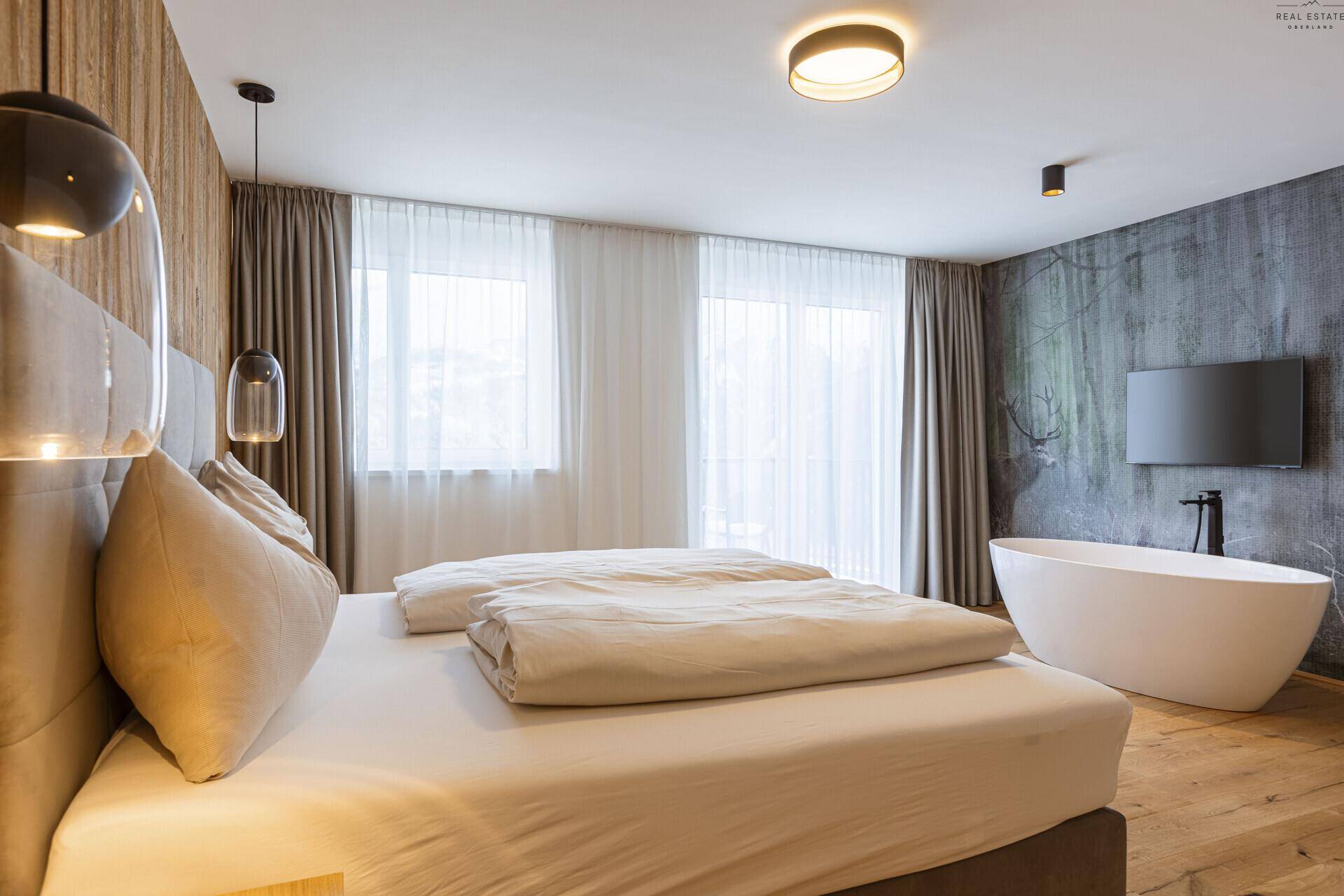 Geräumiges Schlafzimmer mit Doppelbett, Holzwand und freistehender Badewanne.
