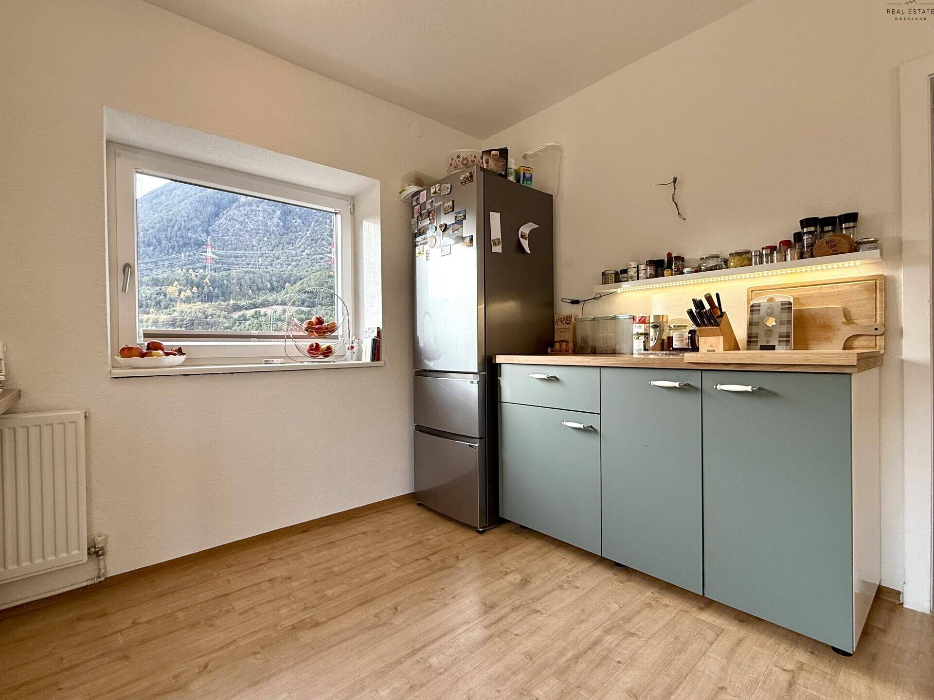 Küche mit Kühlschrank, hellblauen Unterschränken und Fenster mit Bergblick.