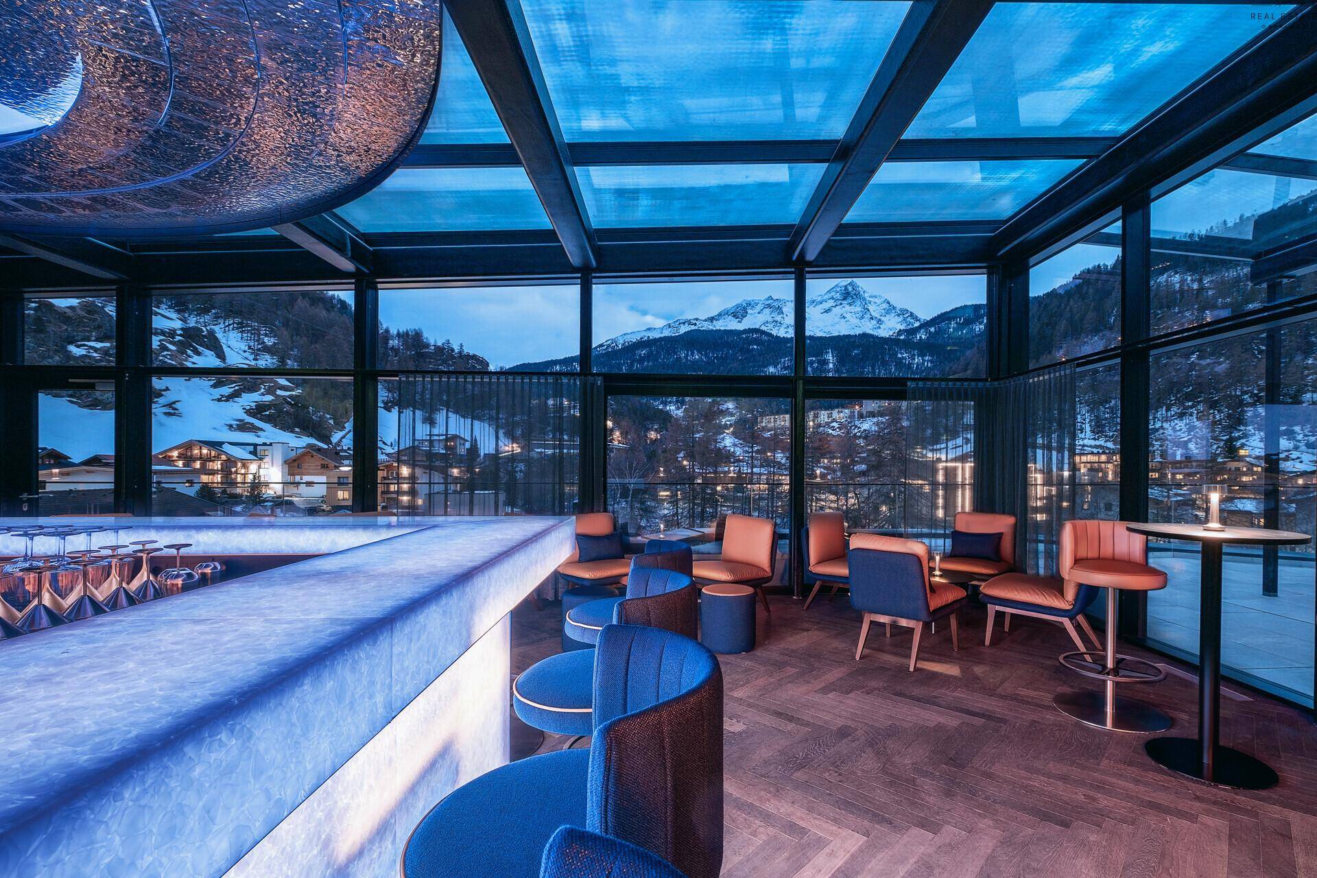 Exklusive Bar mit blauer Beleuchtung, Panoramablick auf die Berge und stilvollen Sitzgelegenheiten.