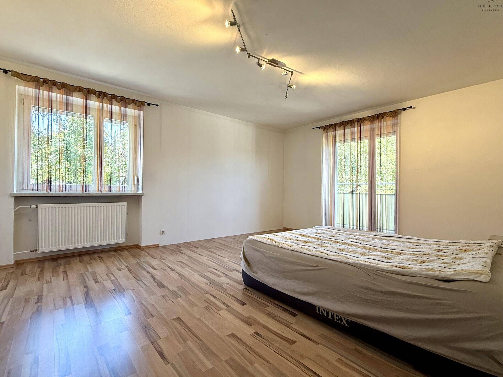 Helles Schlafzimmer mit Laminatboden, großem Fenster und Zugang zum Balkon.