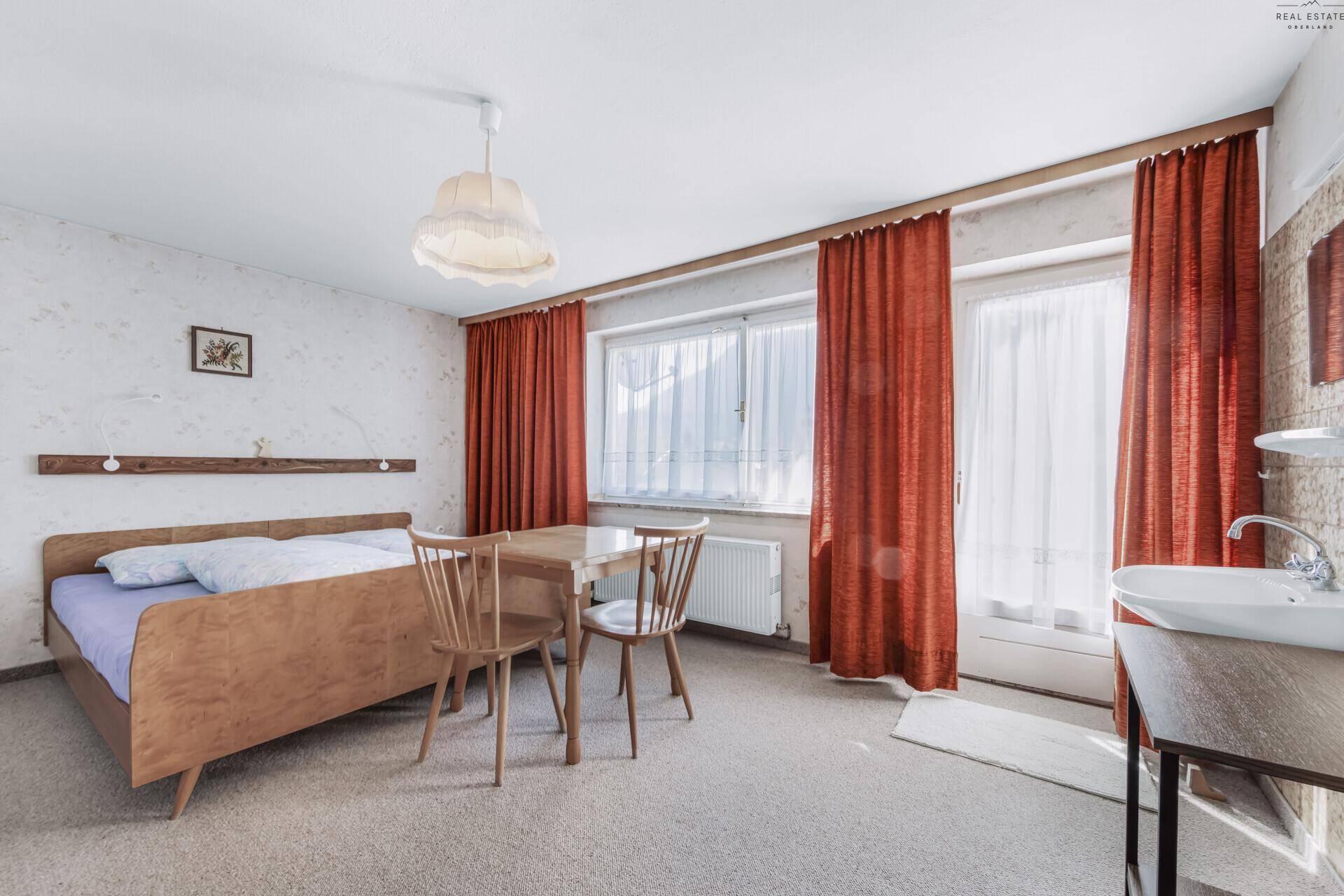 Schlafzimmer mit Einzelbett, Holztisch und Stühlen, sowie einem Waschbecken im Zimmer.