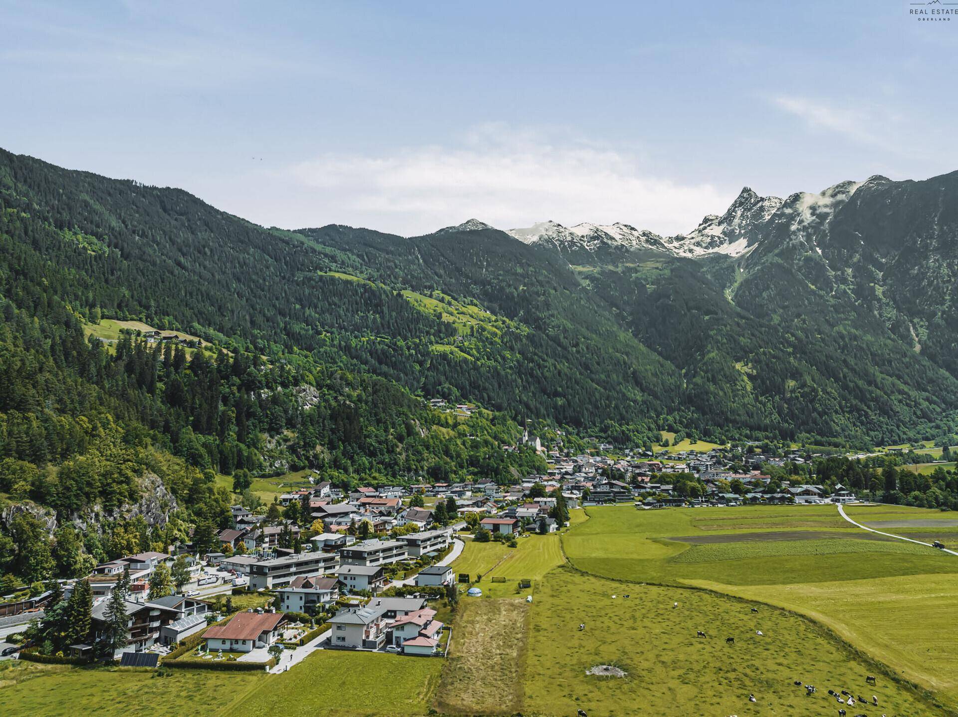 Panoramablick auf ein malerisches Dorf in einem Tal, umgeben von majestätischen Bergen.