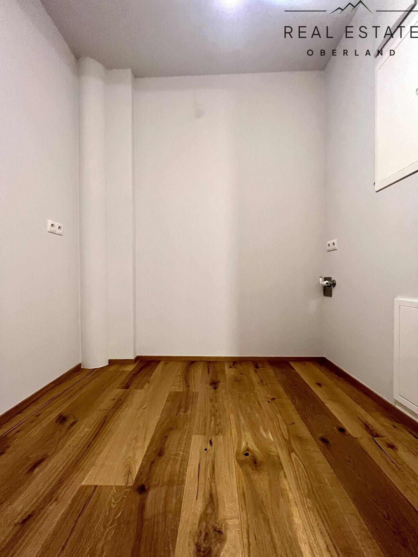 Praktischer Hauswirtschaftsraum mit Holzfußboden und Anschlüssen für Waschmaschine oder Trockner.