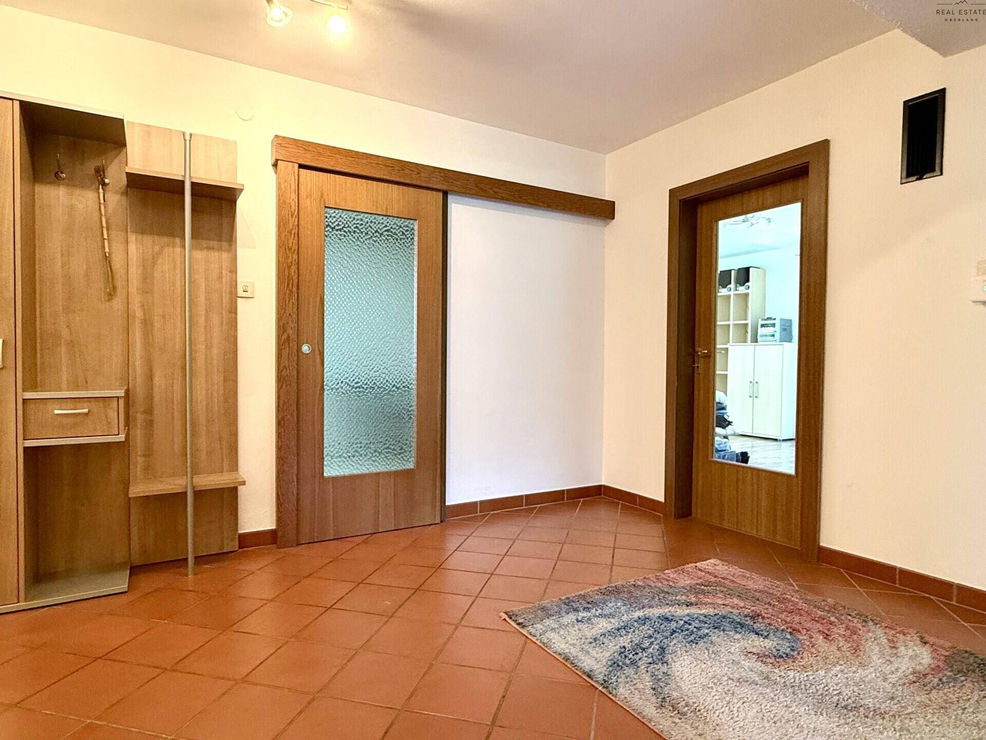 Eingangsbereich mit Terrakotta-Fliesen, Garderobe und Schiebetüren aus Holz und Glas.