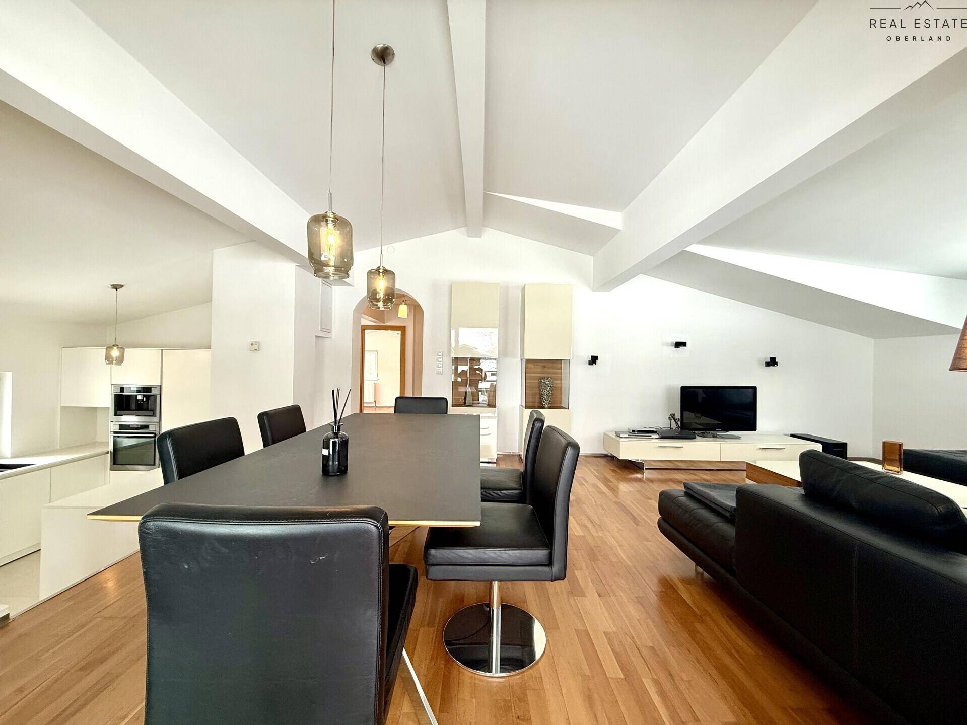 Heller, offener Wohn- und Essbereich mit Holzboden, modernen Möbeln und sichtbaren Deckenbalken.