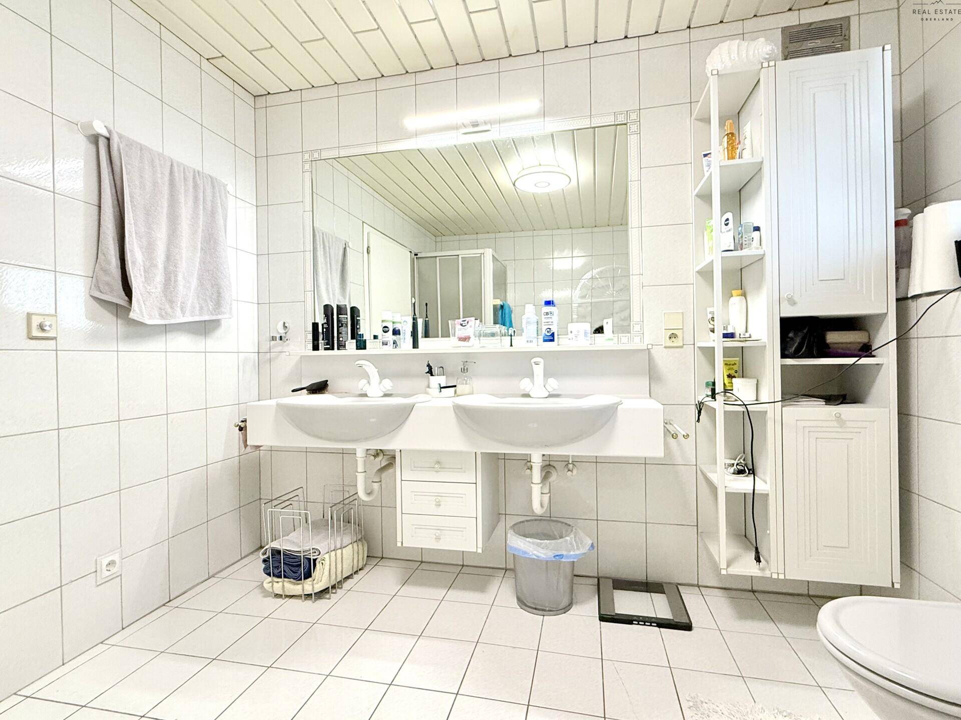 Helles Badezimmer mit Doppelwaschbecken, weißen Fliesen und großem Spiegel.