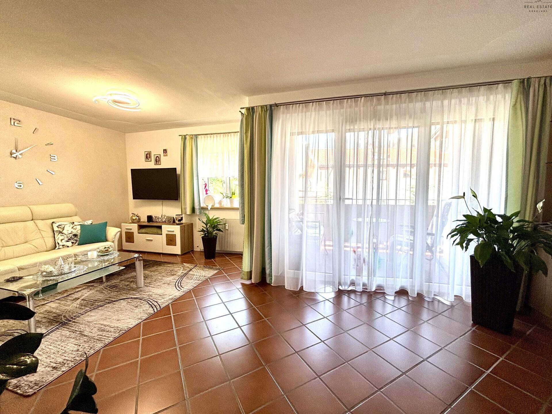 Lichtdurchflutetes Wohnzimmer mit Zugang zum Balkon, Terrakottafliesen und großen Fenstern.