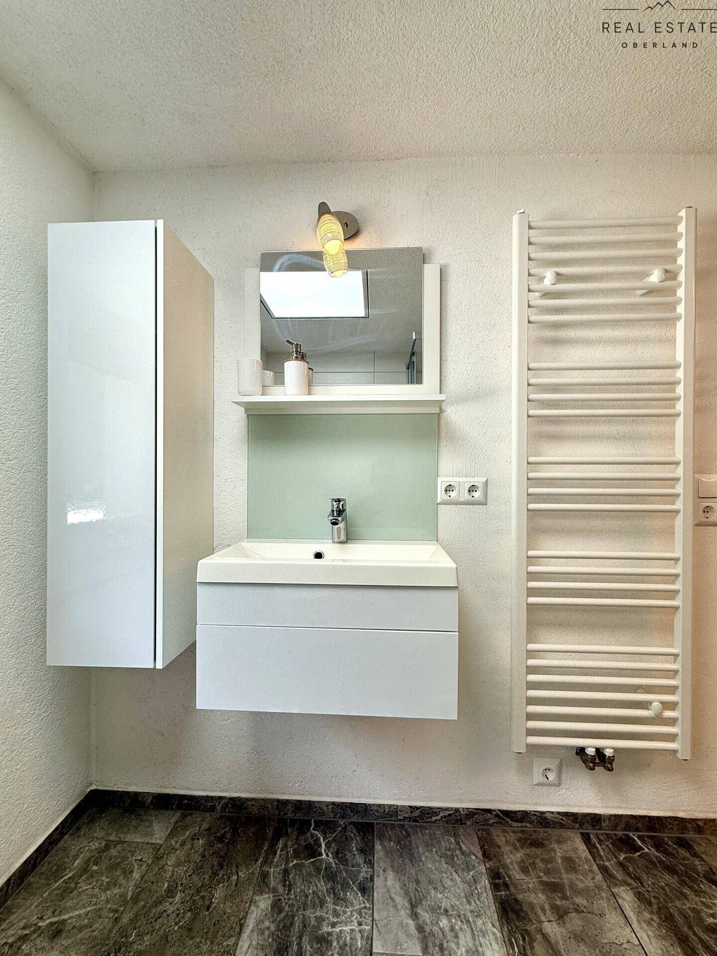 Modernes Badezimmer mit Waschtisch, Spiegelschrank und beheiztem Handtuchhalter.