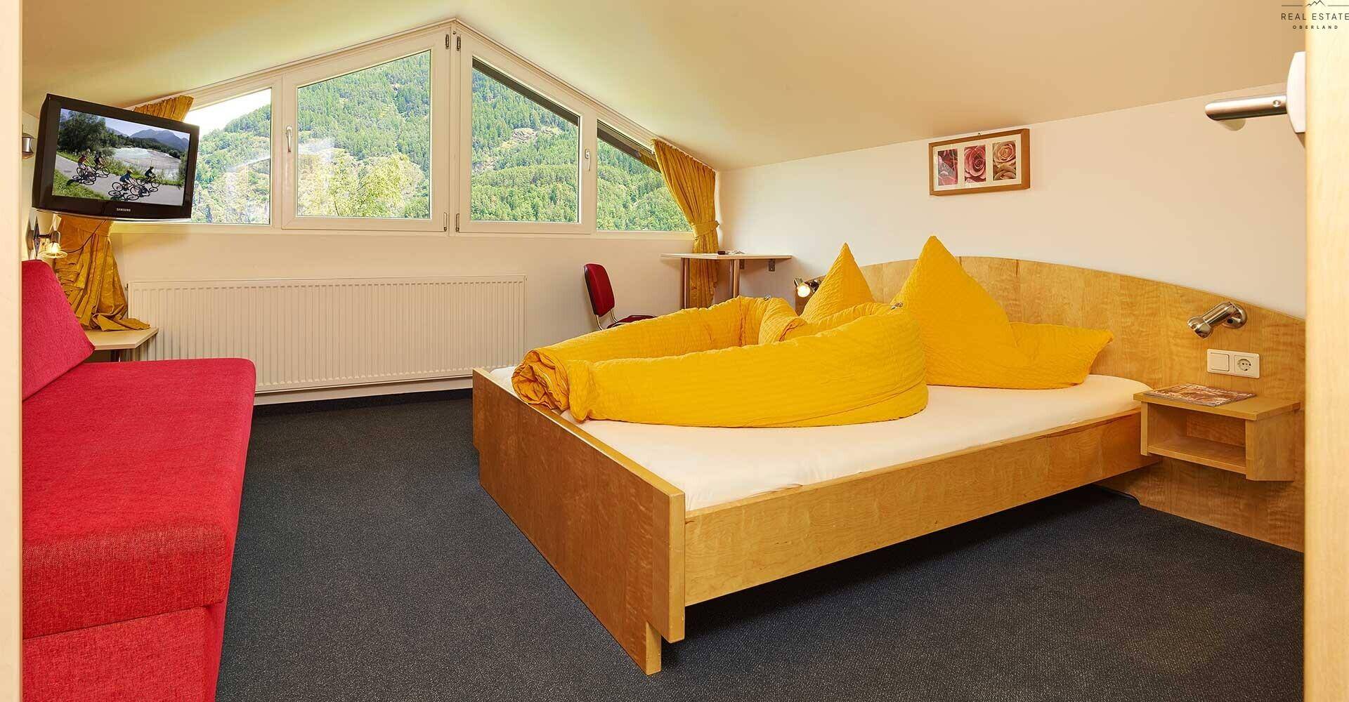 Schlafzimmer im Dachgeschoss mit schrägen Fenstern, Doppelbett und Blick auf die Berge.