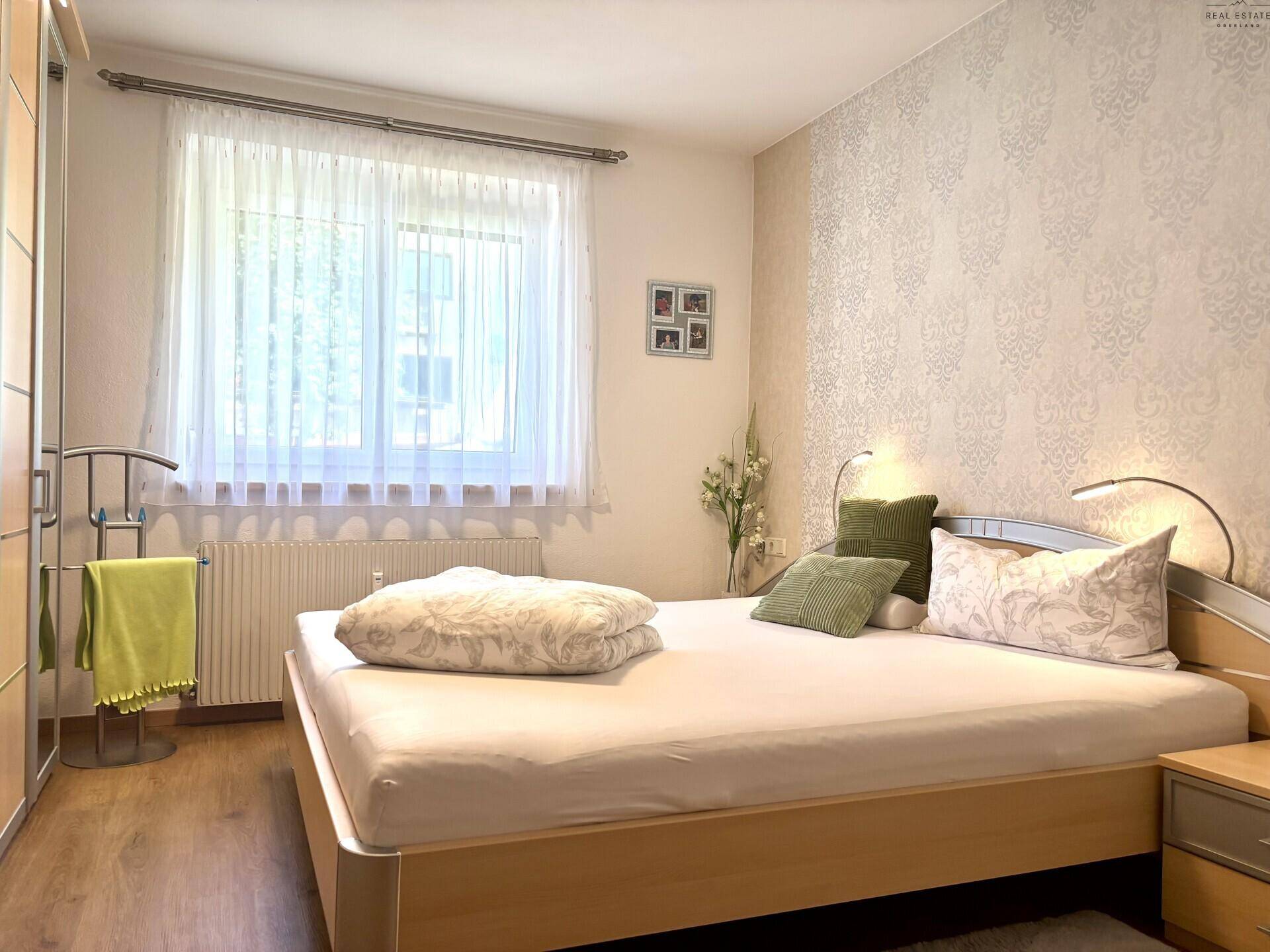 Helles Schlafzimmer mit Doppelbett, Holzrahmen und gemusterter Tapete, gut beleuchtet.