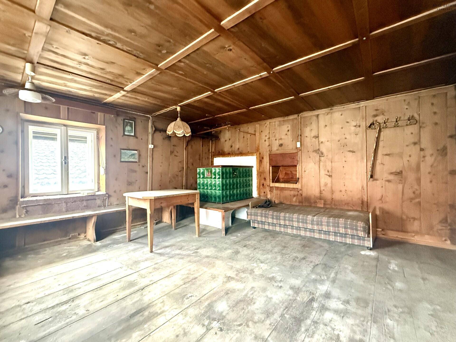 Traditioneller Wohnraum mit Holzwänden, Holzboden und grünem Kachelofen, bereit zur Renovierung.