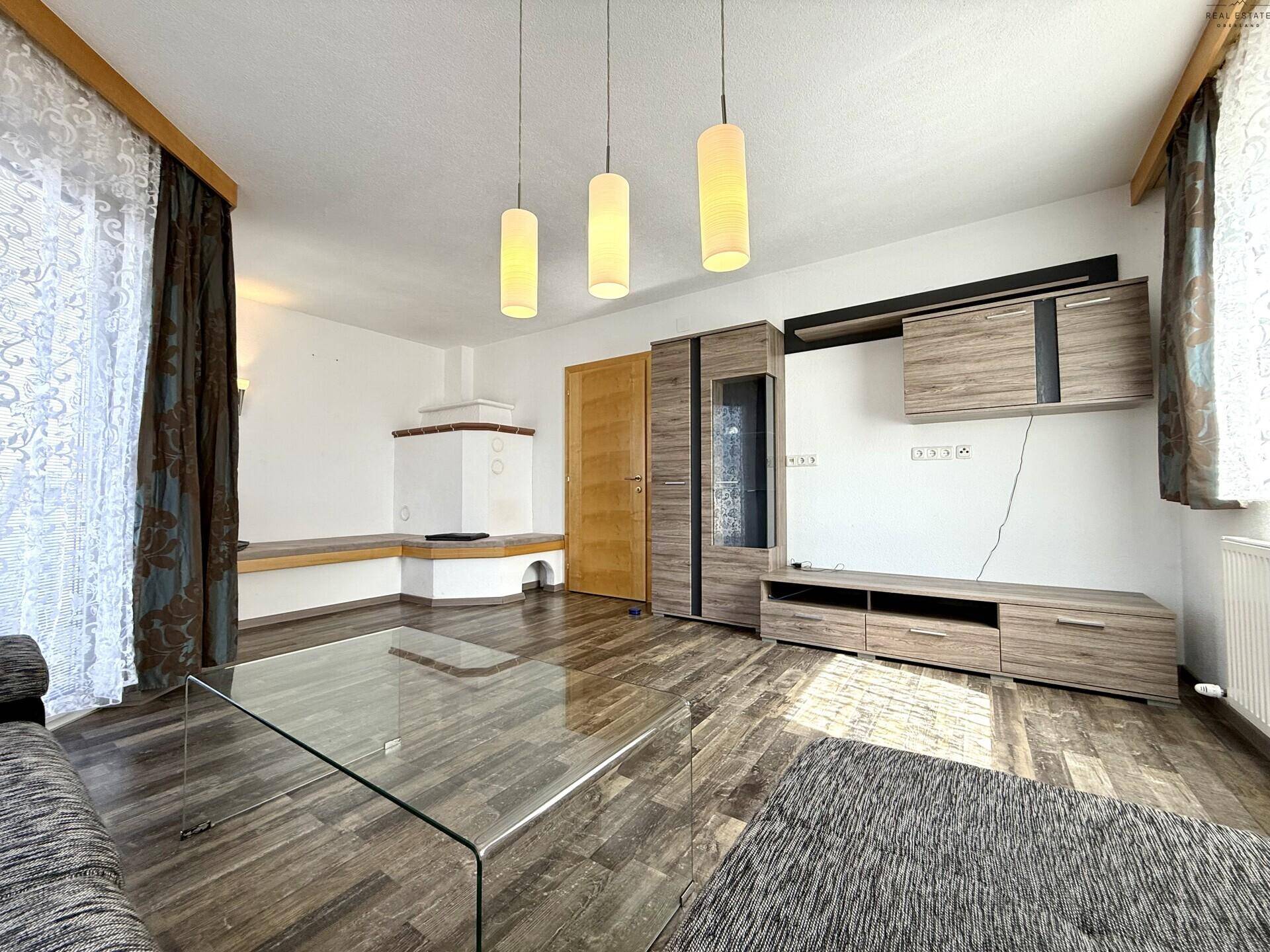 Wohnzimmer mit modernem Mediamöbel, Holzboden und traditionellem Kachelofen.