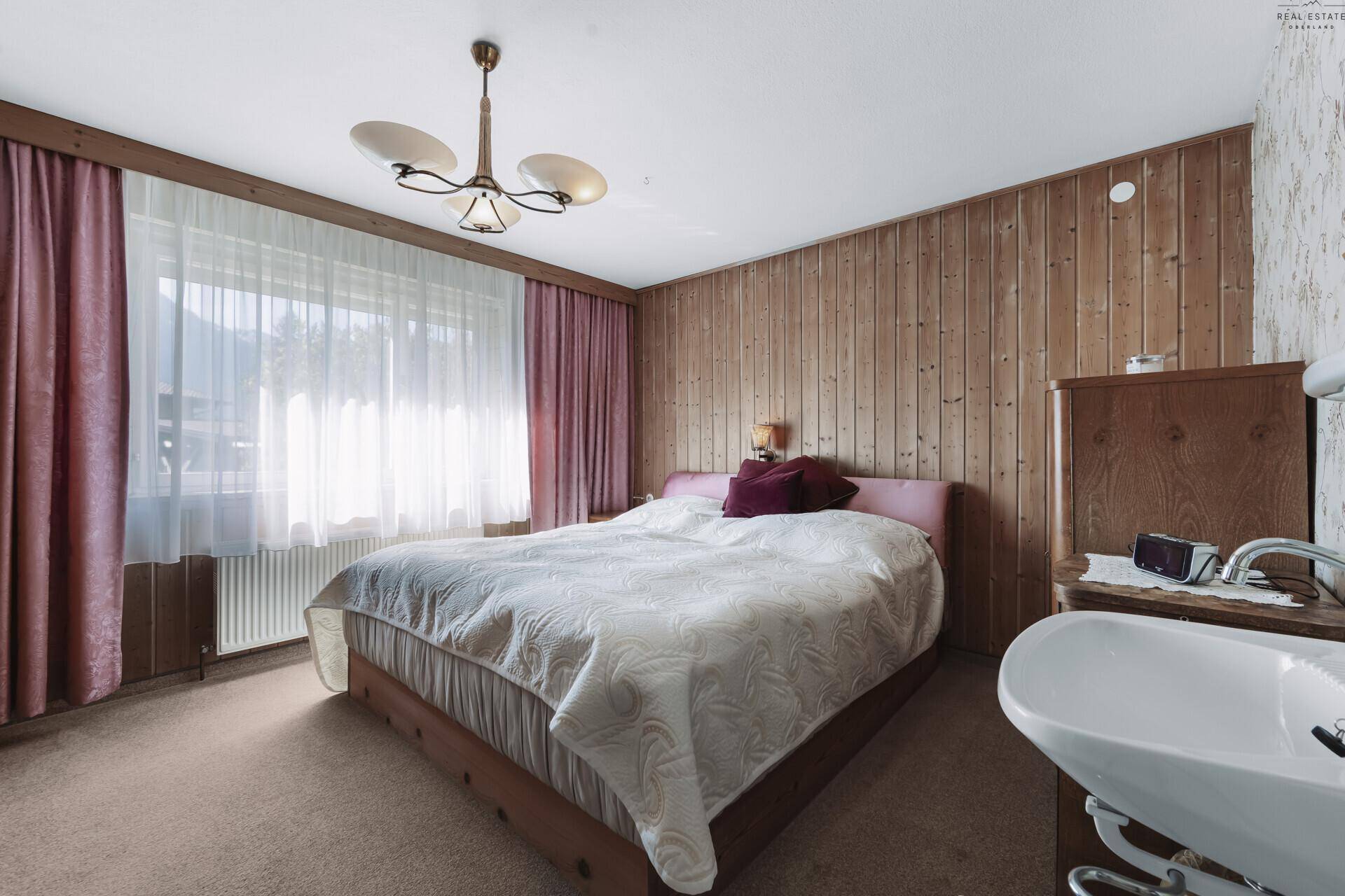 Schlafzimmer mit Doppelbett, Holzvertäfelung und traditioneller Deckenleuchte.