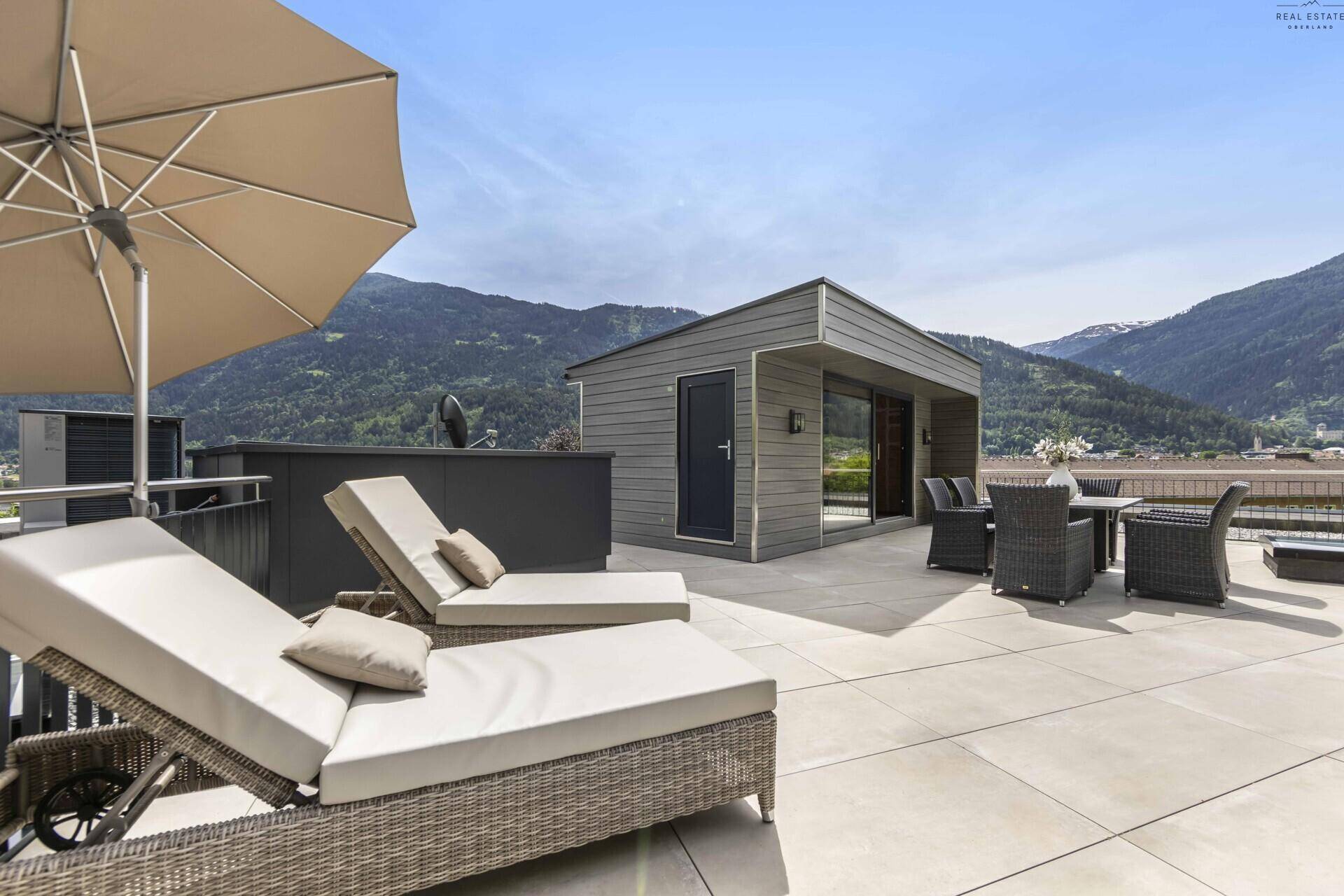 Dachterrasse mit Liegestühlen und Essbereich, bietet einen weiten Blick auf die umliegende Bergwelt.