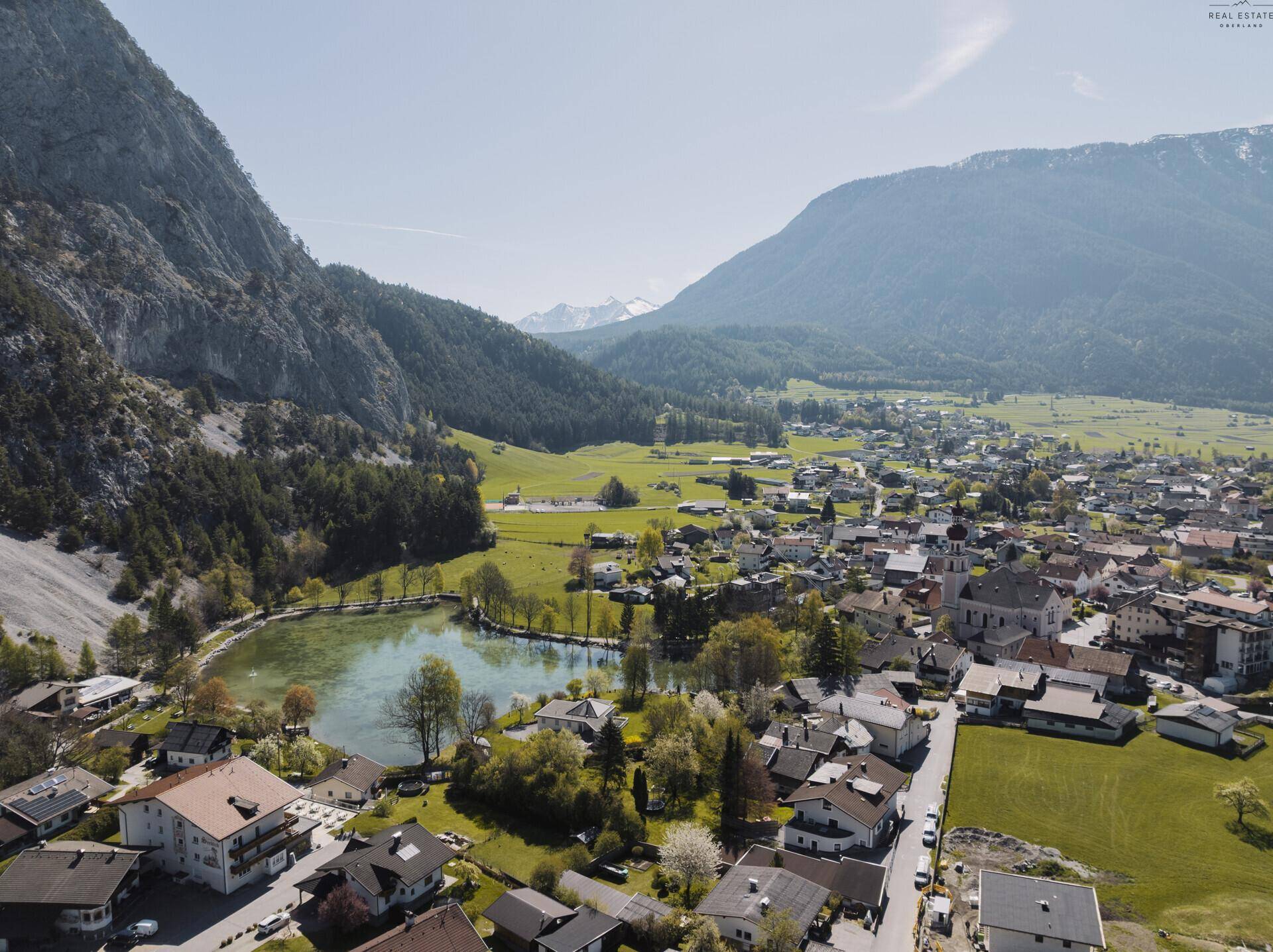 Panoramablick aus der Vogelperspektive auf das Dorf mit See und umliegender Berglandschaft.