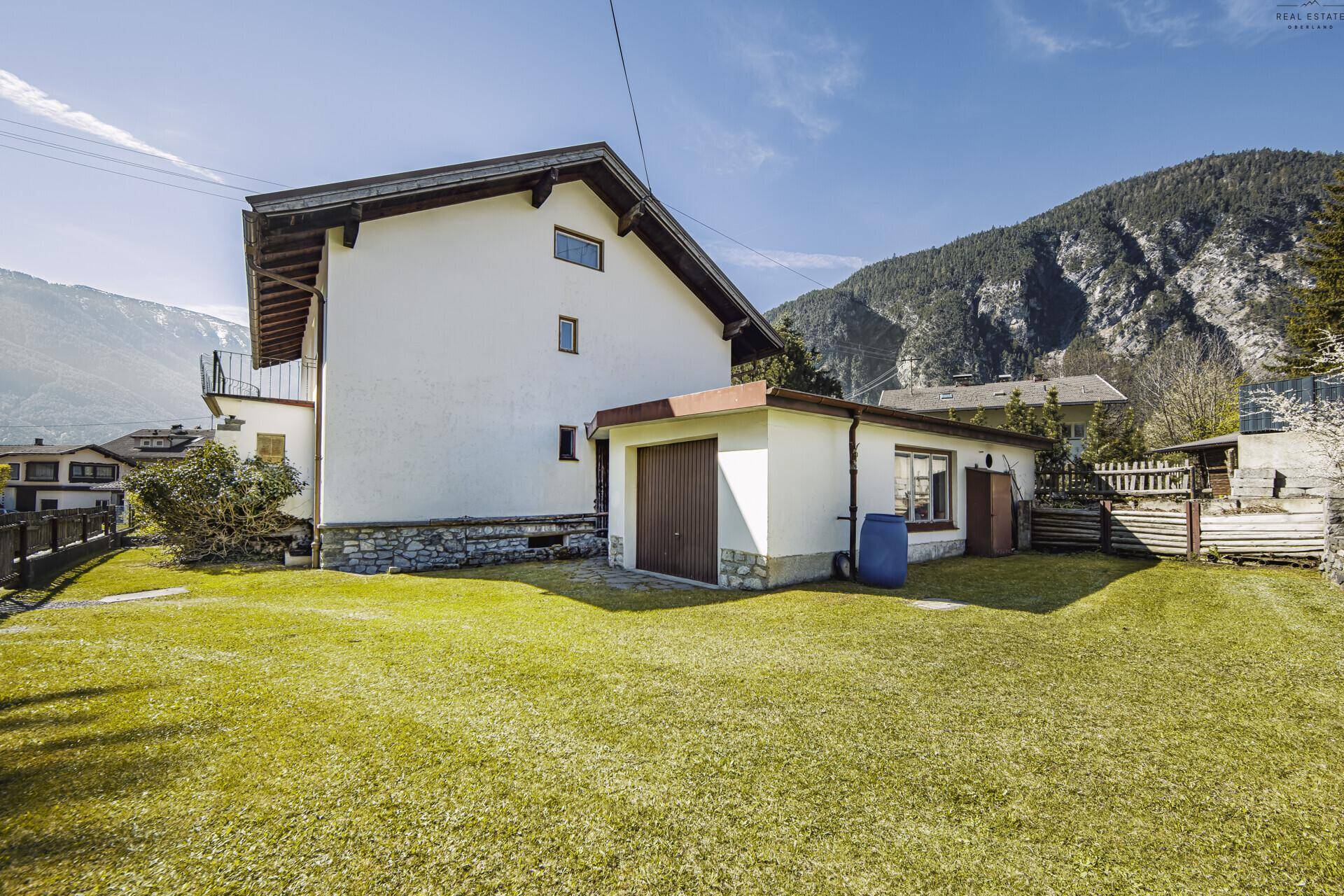 Hausfassade mit angrenzender Garage und großem Gartenbereich.