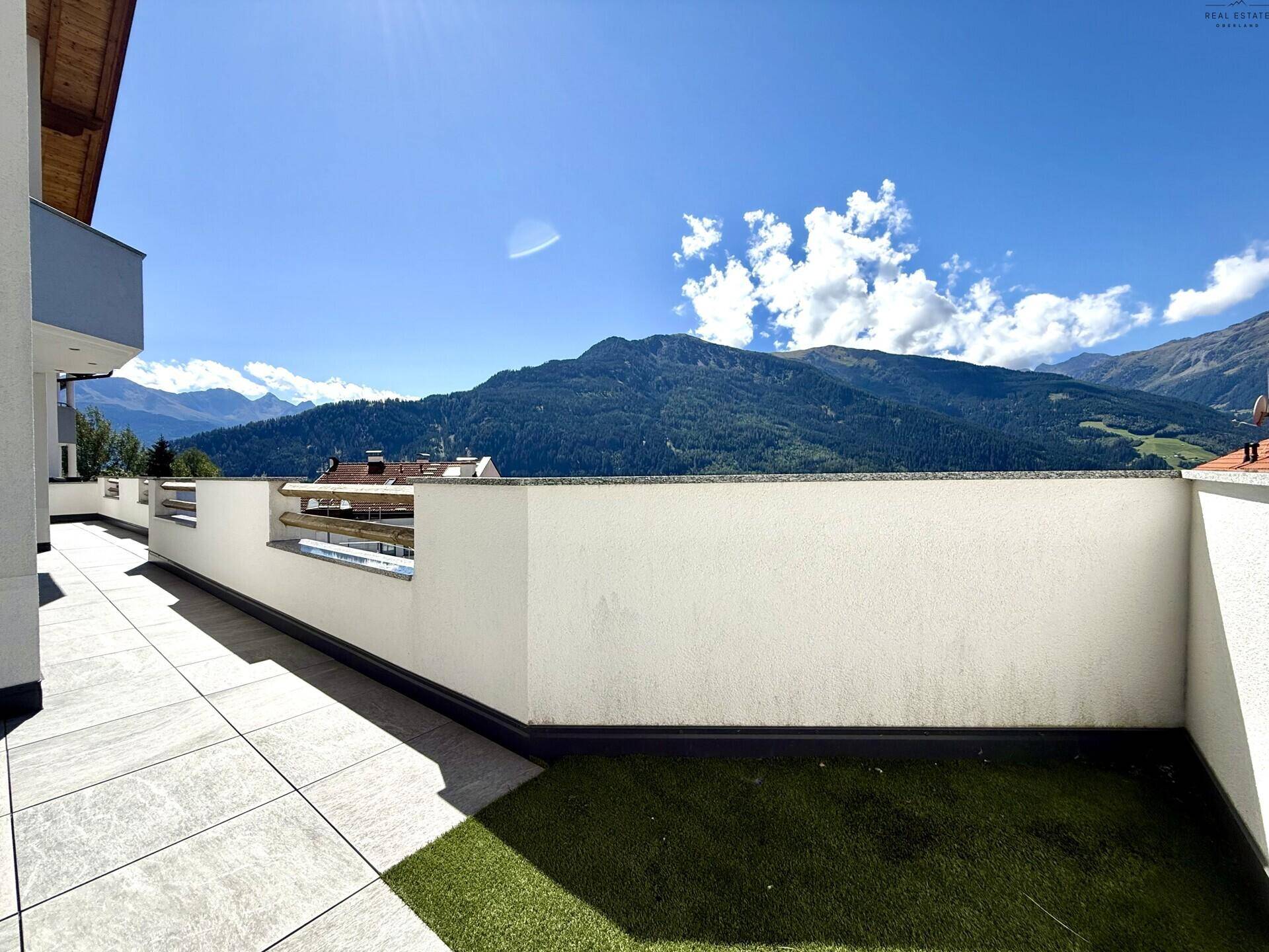 Weitläufige Terrasse mit Kunstrasen und Panoramablick auf die umliegende Berglandschaft.