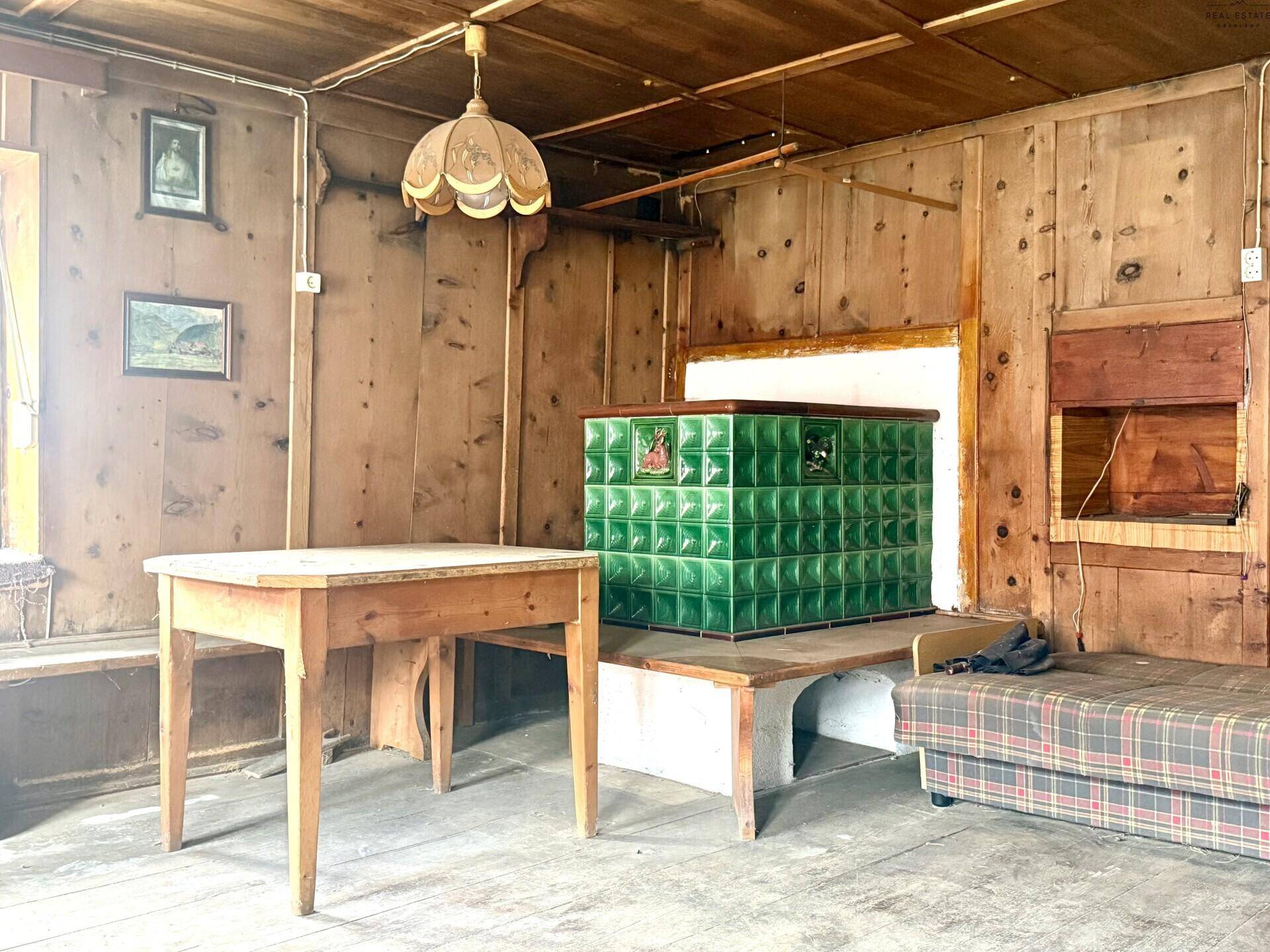 Detailansicht des grünen Kachelofens in einem rustikalen Wohnzimmer mit Holzelementen.