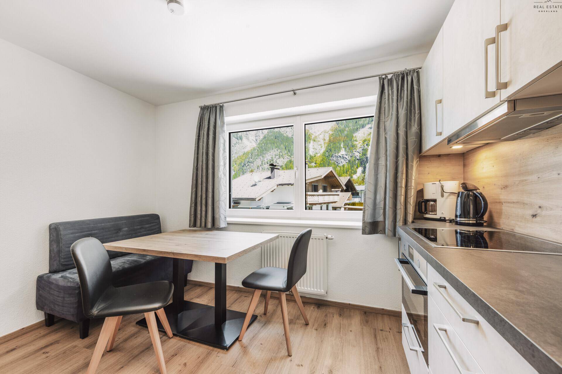 Moderne Küche mit Essbereich, Holzboden und Fensterblick auf die umliegenden Berge.