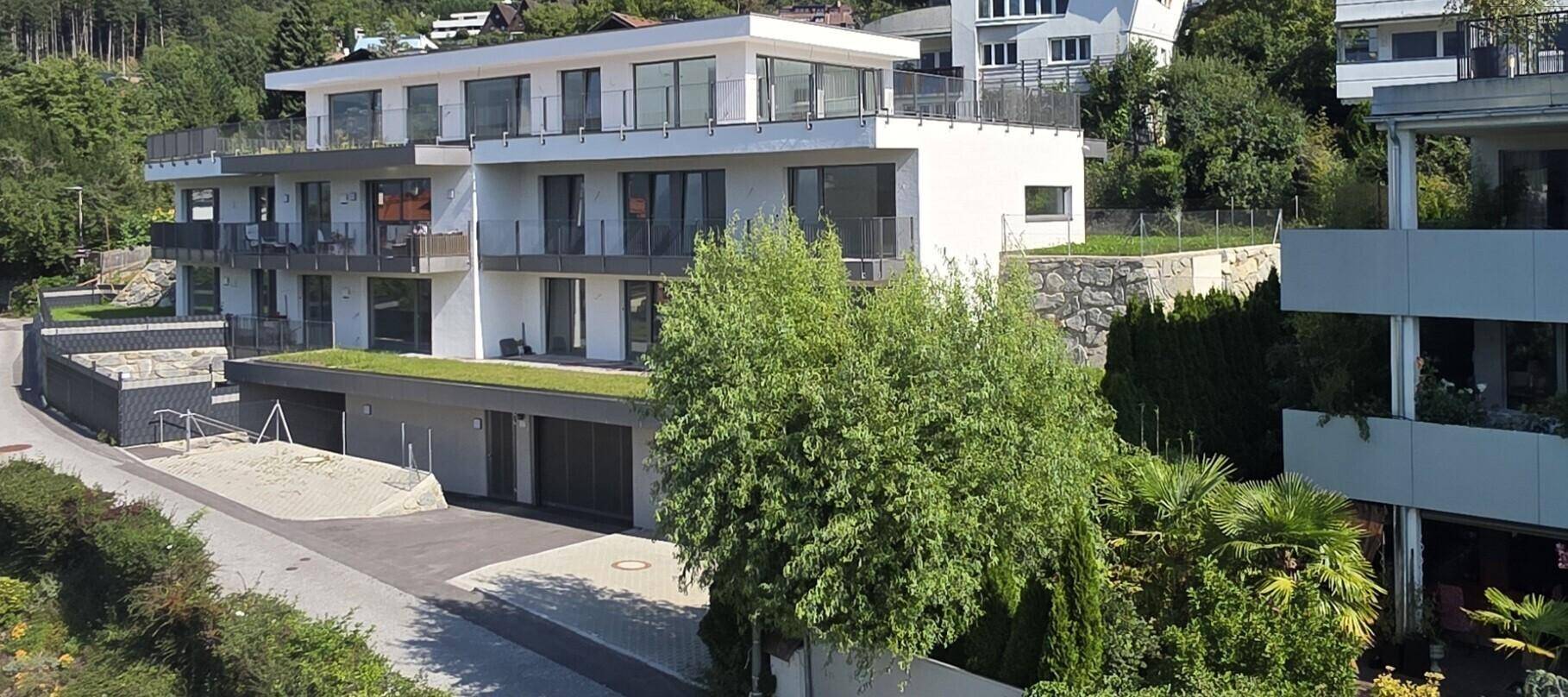 Modernes Wohngebäude mit mehreren Etagen, Balkonen und begrüntem Dach in grüner Umgebung.