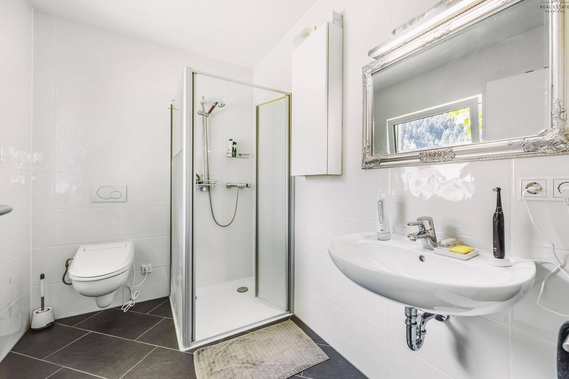Modernes Badezimmer mit Duschkabine, wandhängendem WC und großem Spiegel.