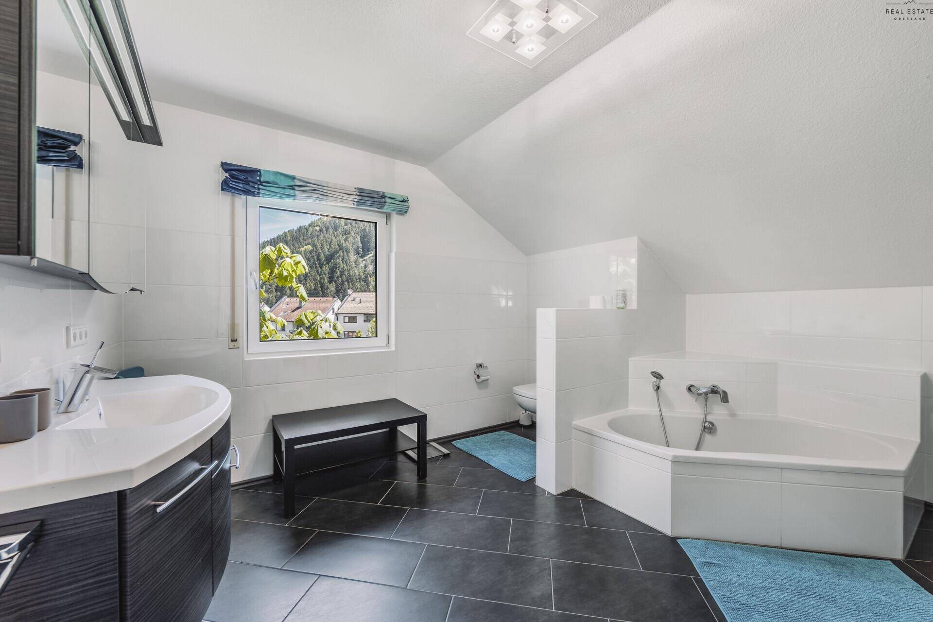 Badezimmer im Dachgeschoss mit Badewanne, Waschbecken und Fenster mit Bergblick.