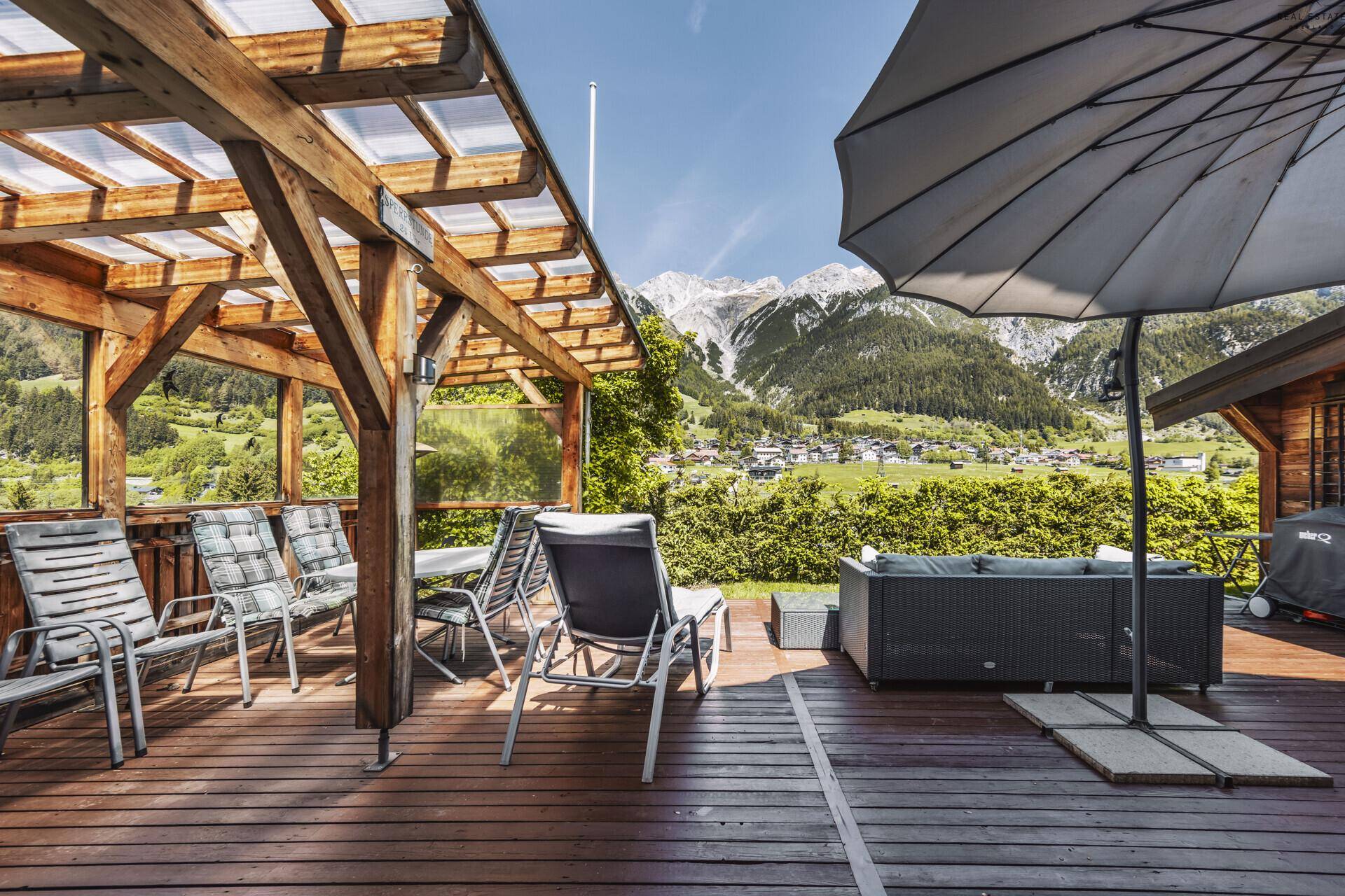 Geräumige Holzterrasse mit überdachtem Bereich und Sitzgelegenheiten, umgeben von Bergen.