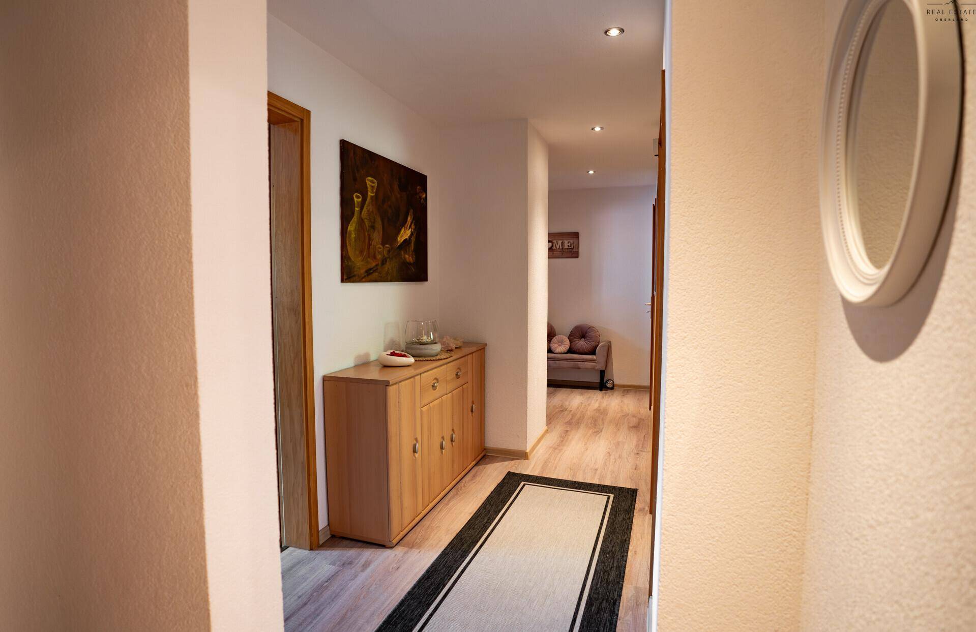 Heller Flur mit Holzkommode, Spiegel und Laminatboden, der zu weiteren Räumen führt.
