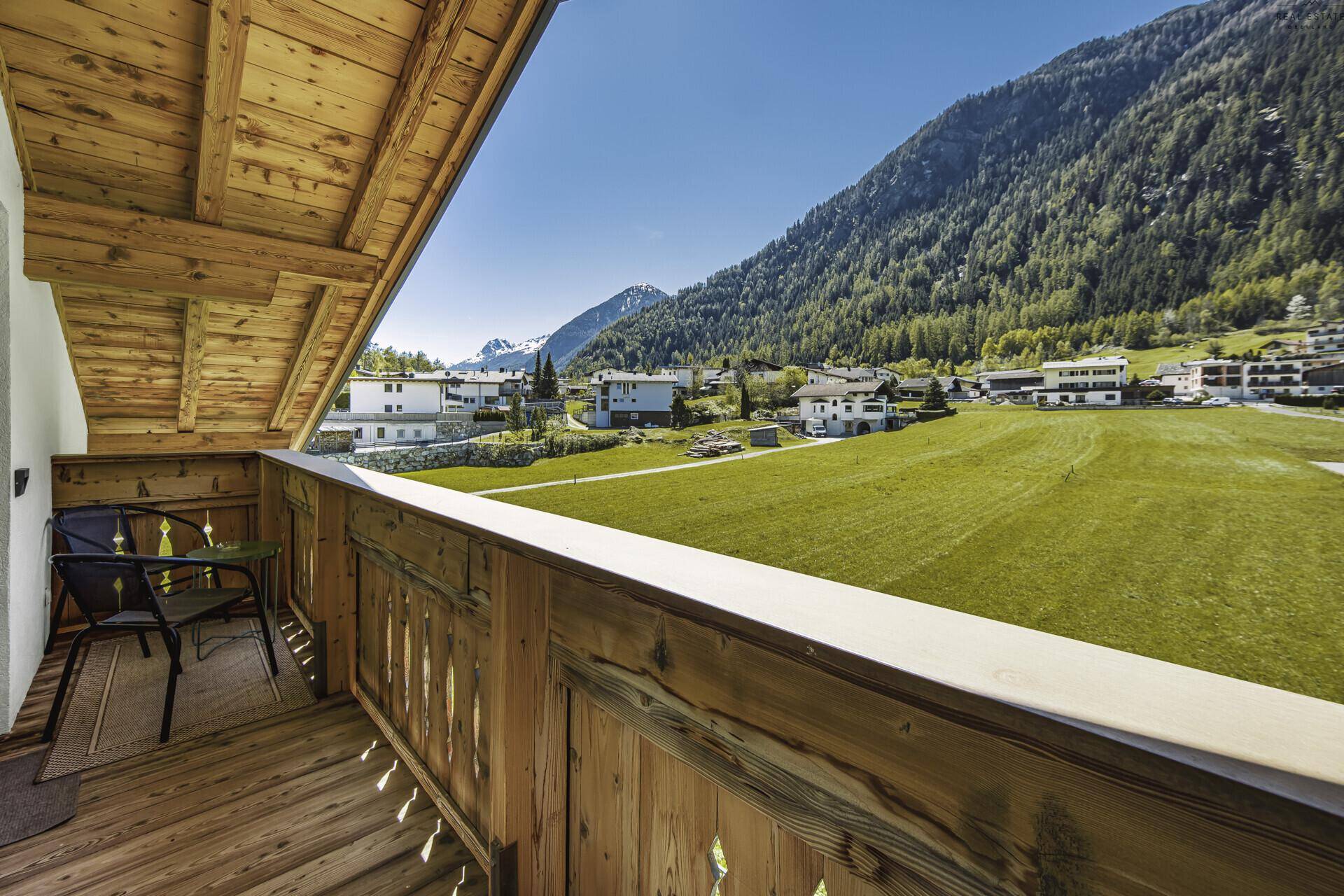Geräumiger Holzbalkon mit Sitzgelegenheiten und weitem Blick auf die grüne Berglandschaft.