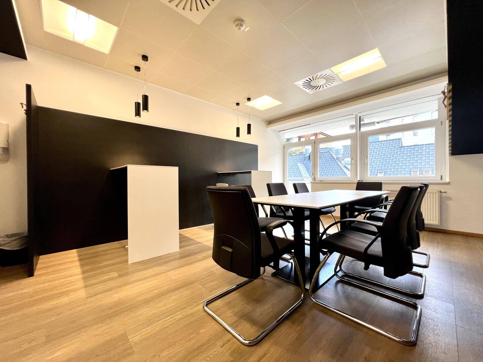 Moderne Büroküche mit schwarzer Wandverkleidung, Holzboden und einem Besprechungstisch.
