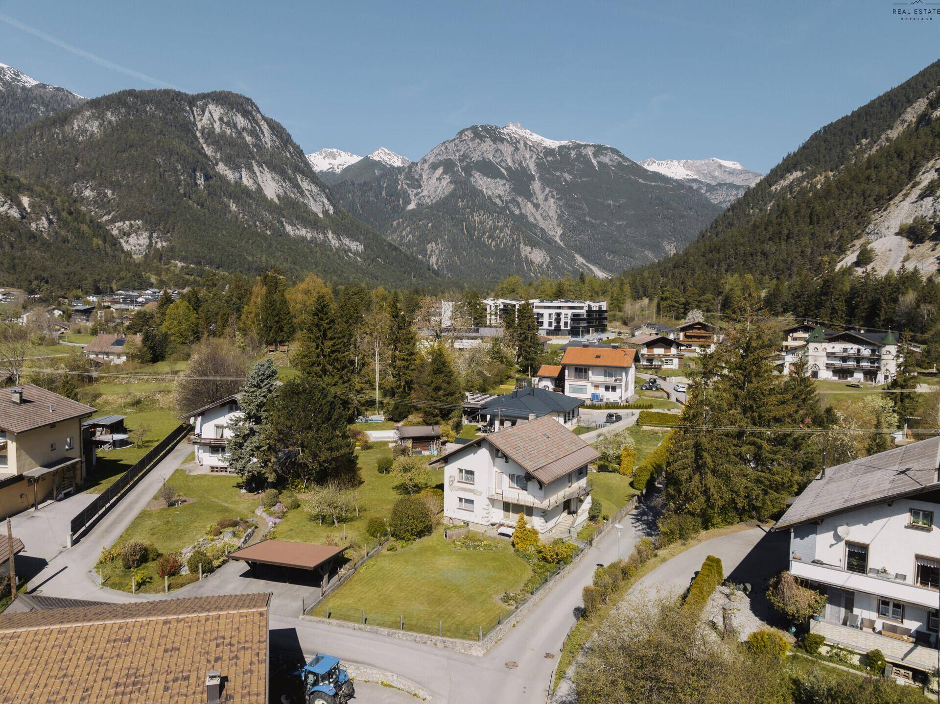 Weitläufige Luftaufnahme der Siedlung mit Häusern und Bergen im Hintergrund.