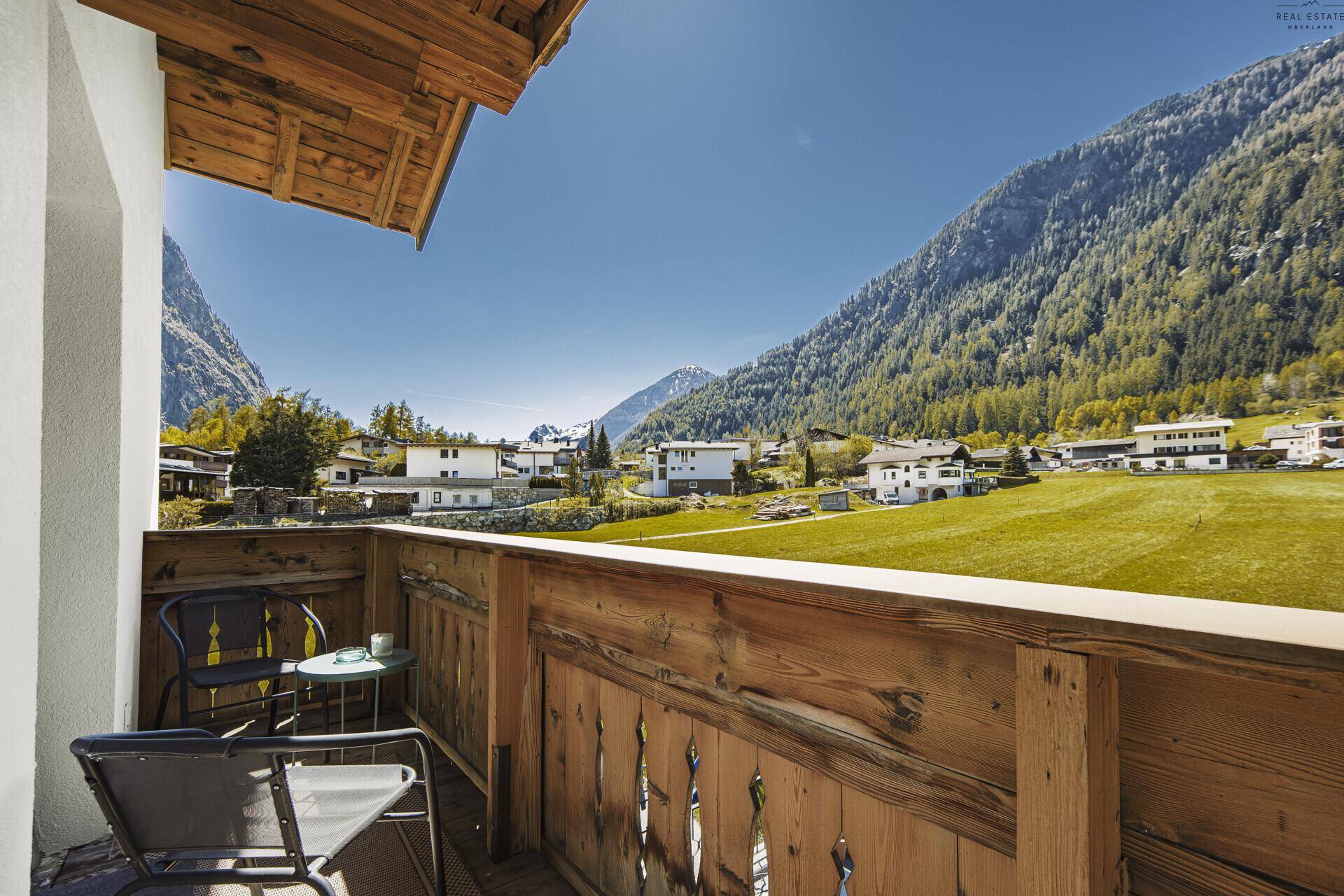 Gemütlicher Holzbalkon mit Sitzgelegenheiten und weitem Blick auf die grüne Berglandschaft.