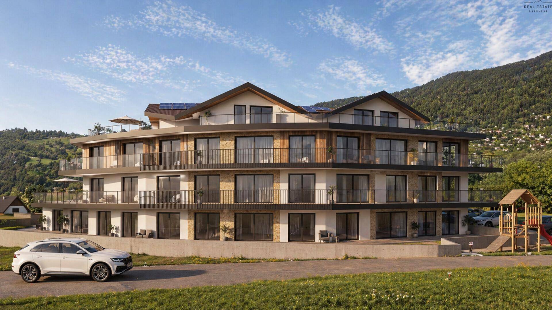 Moderne Wohnanlage mit Balkonen, Solaranlagen und einem Spielplatz in alpiner Umgebung.