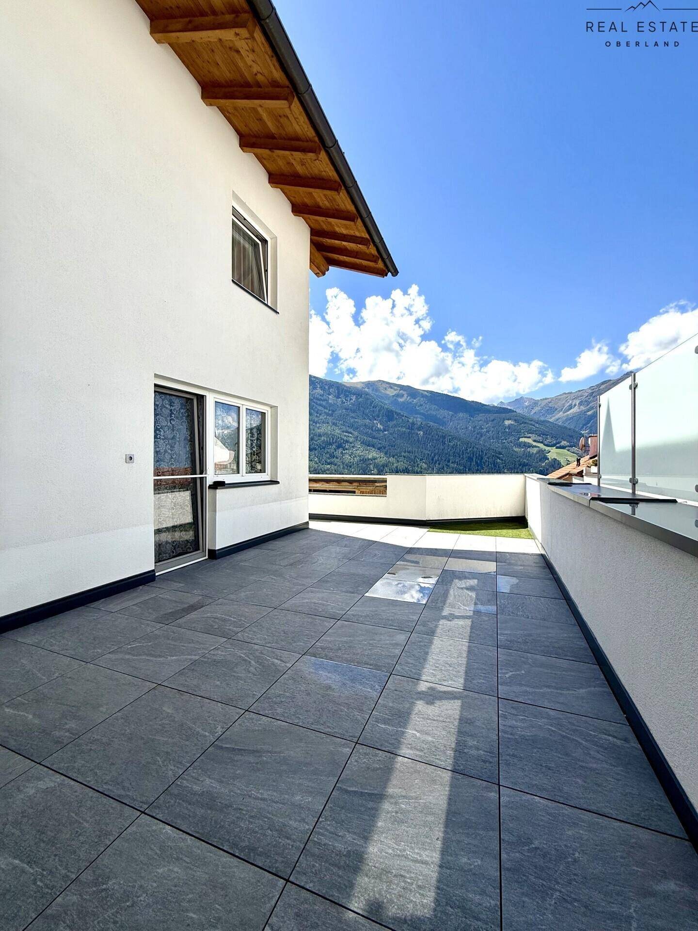 Sonniger Terrassenbereich mit Fliesenboden und weitem Blick auf die Berglandschaft.