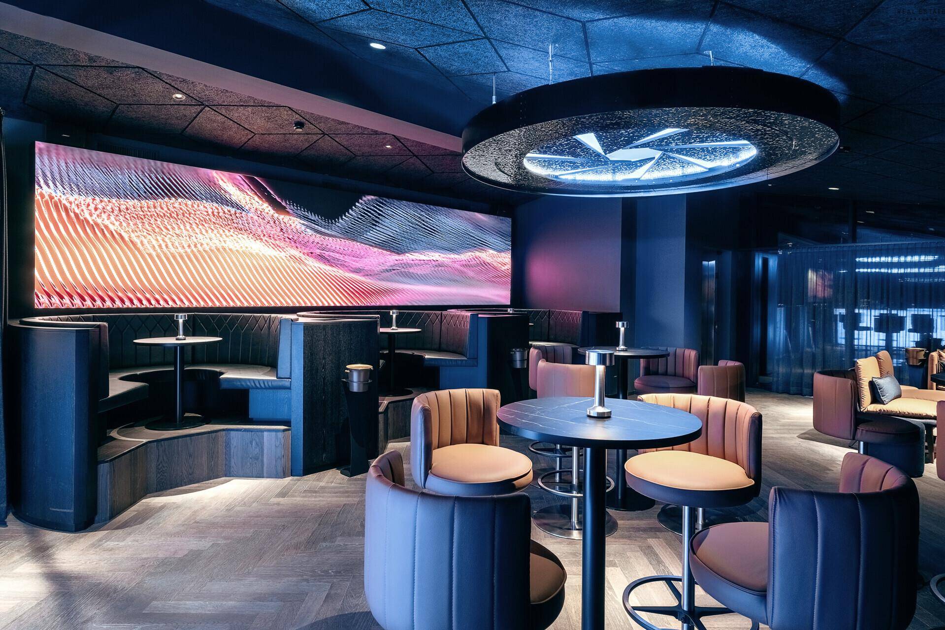 Moderner Loungebereich mit großer LED-Wand, bequemen Sitznischen und stilvoller Beleuchtung.