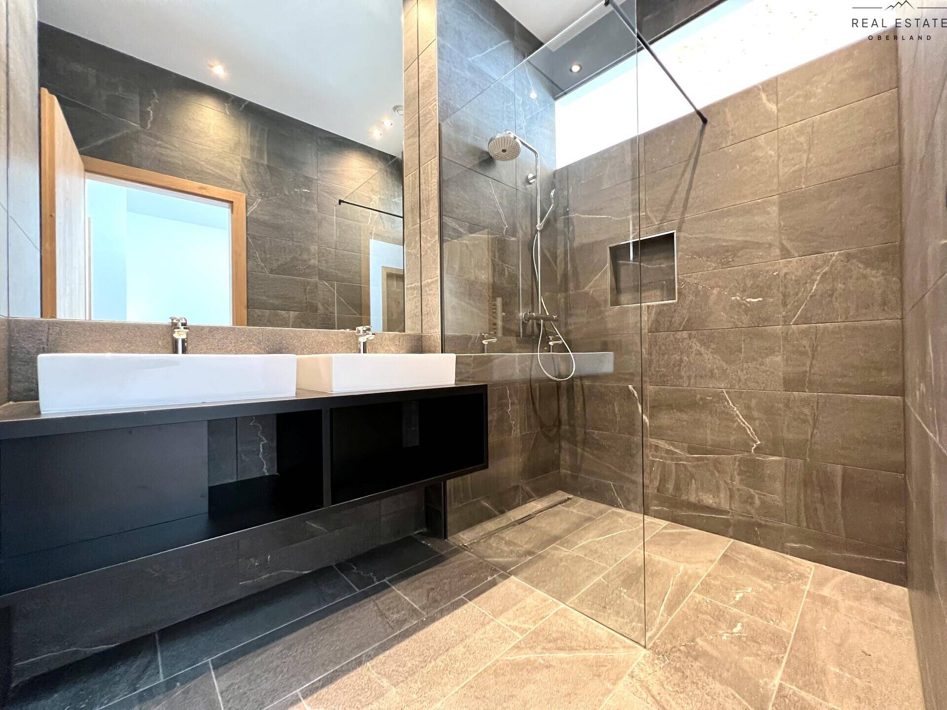 Luxuriöses Badezimmer mit dunklen Fliesen, Doppelwaschbecken und großer begehbarer Regendusche.