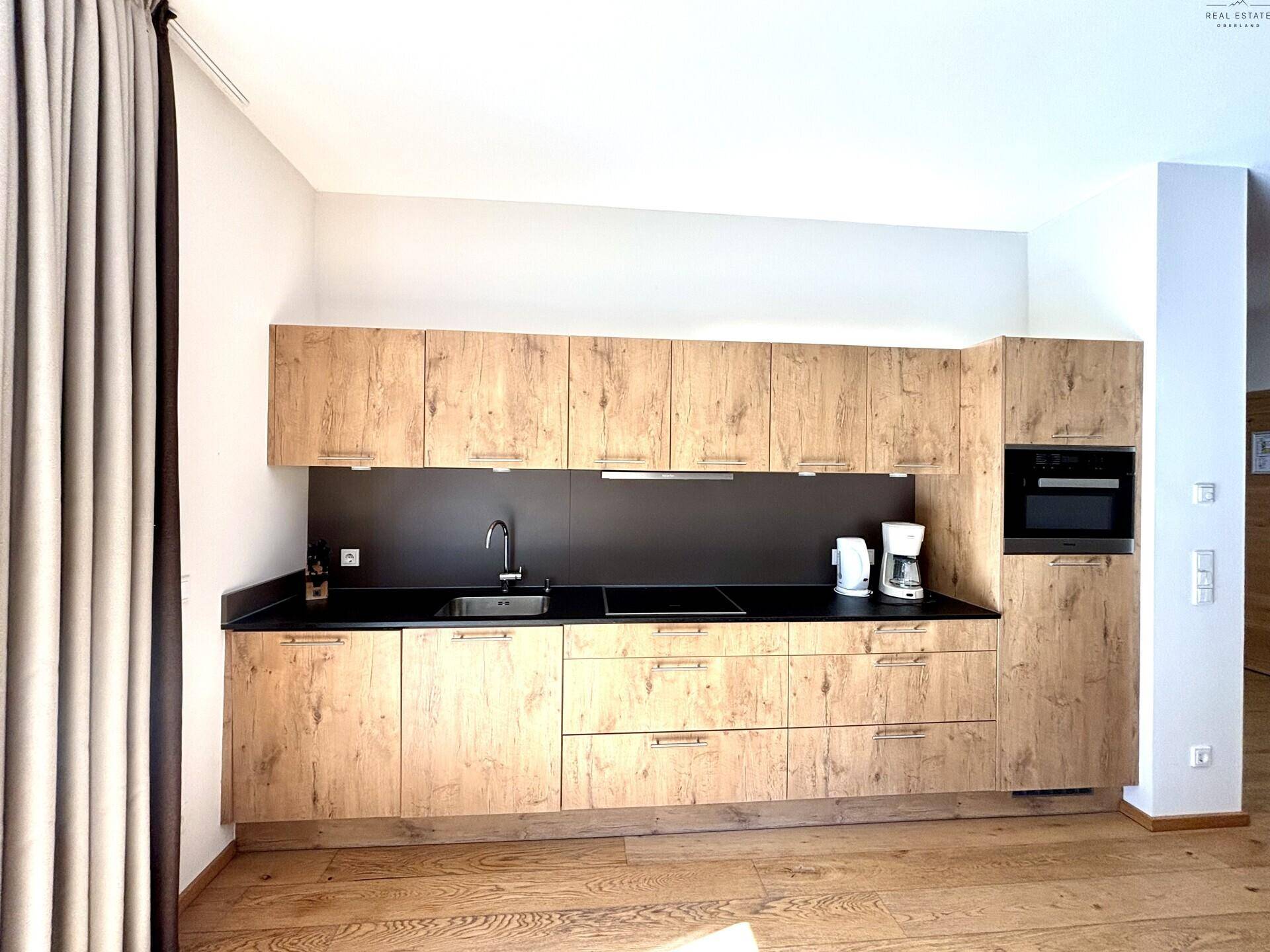 Moderne Einbauküche mit Holzfronten, dunkler Arbeitsplatte und integrierten Geräten.