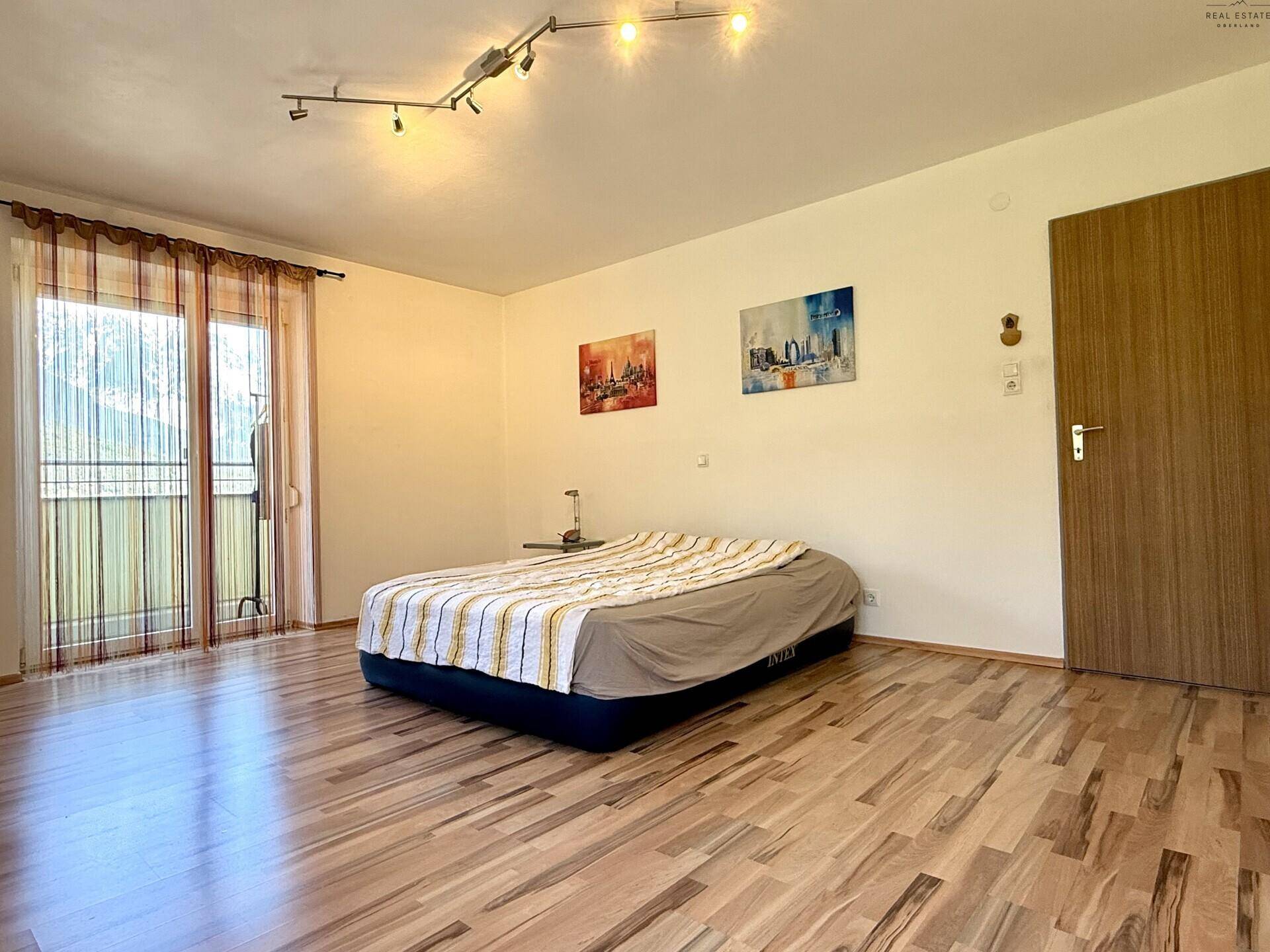 Geräumiges Schlafzimmer mit Laminatboden, Kunstwerken an der Wand und Balkonzugang.
