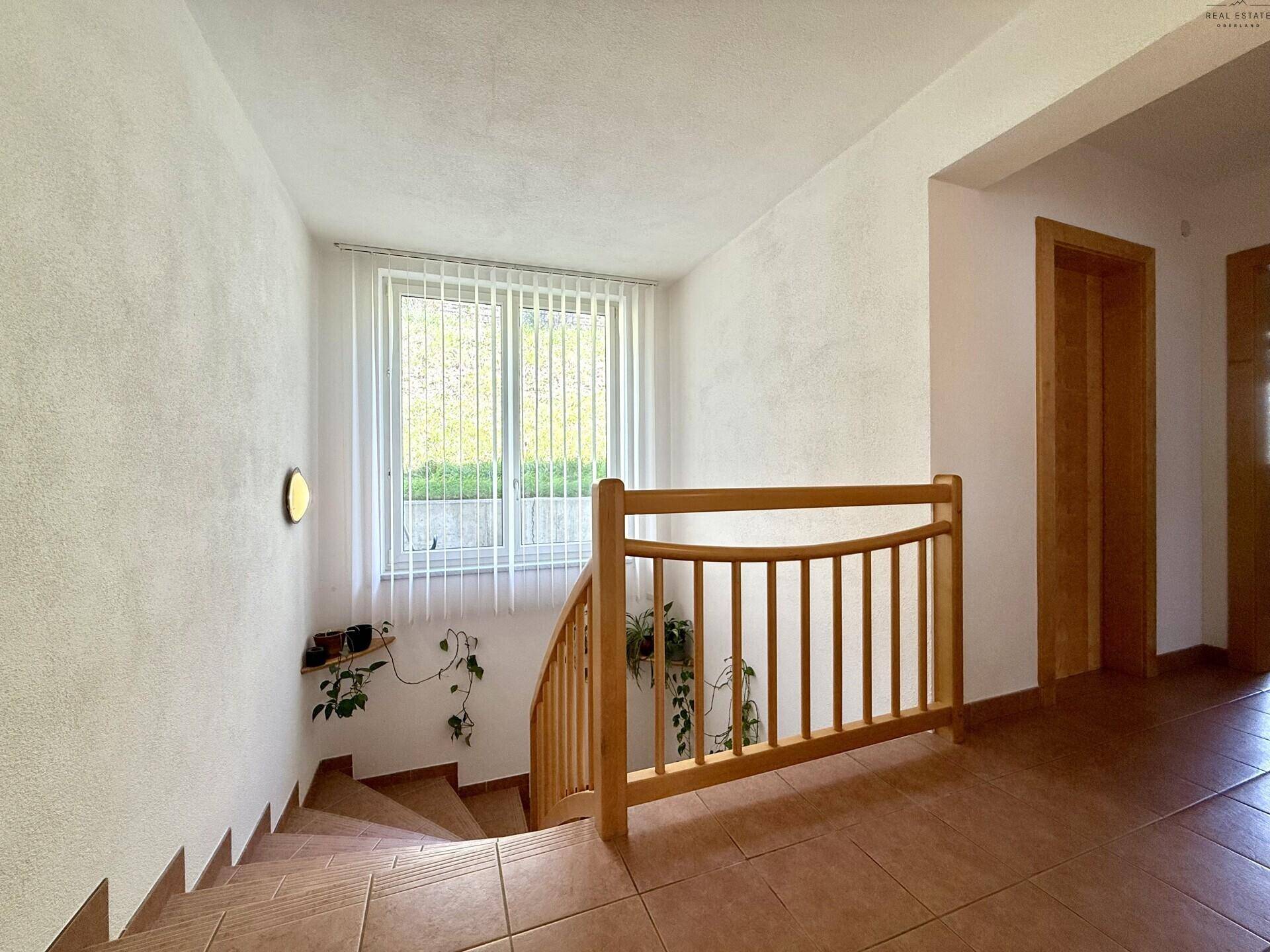 Helles Treppenhaus mit Holzgeländer und gefliesten Stufen, das die Etagen des Hauses verbindet.