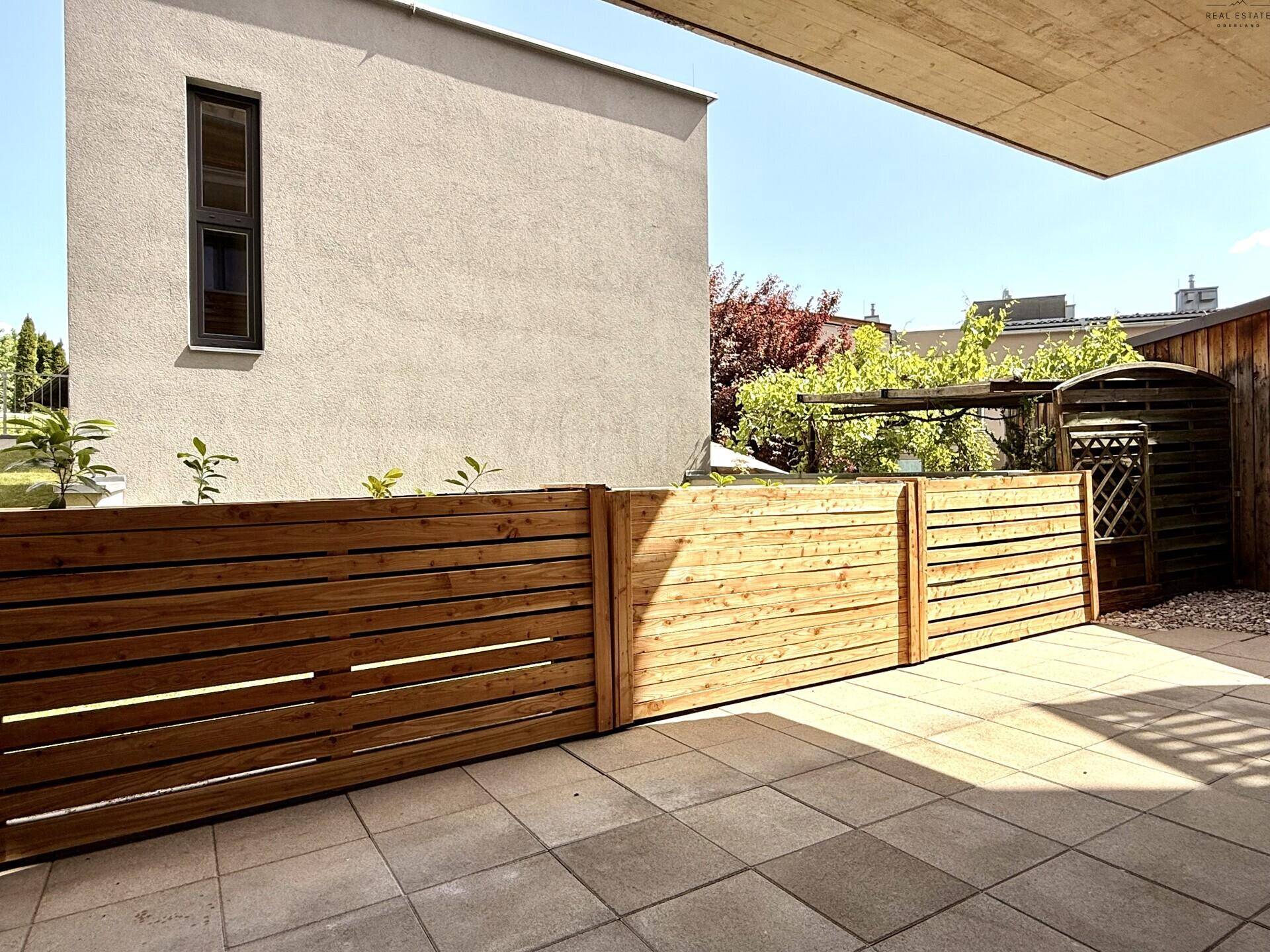 Sonniger Terrassenbereich mit Holzzaun und Blick auf die grüne Umgebung.