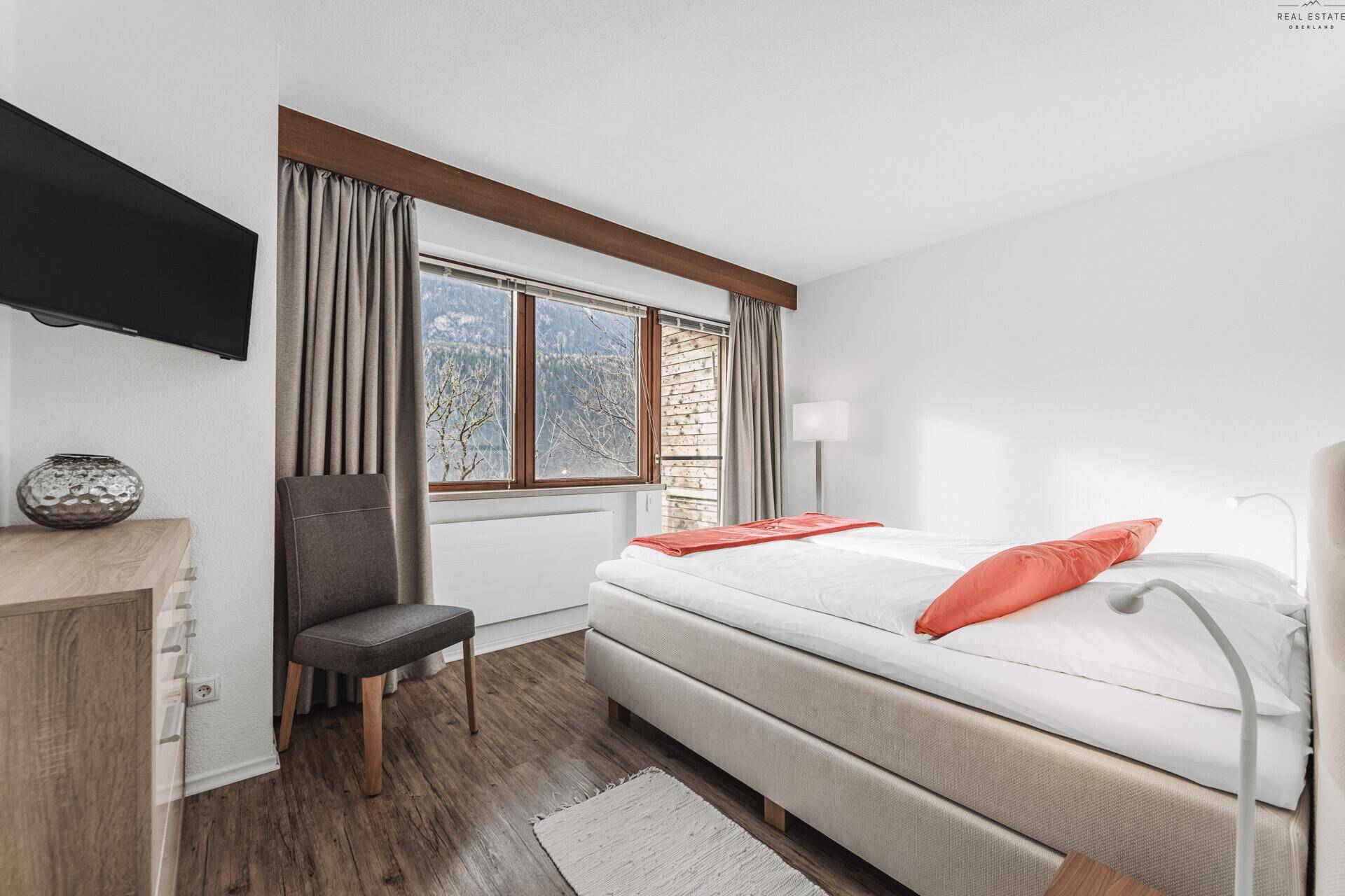 Komfortables Schlafzimmer mit Doppelbett, Holzboden und Fenster mit Blick ins Grüne.