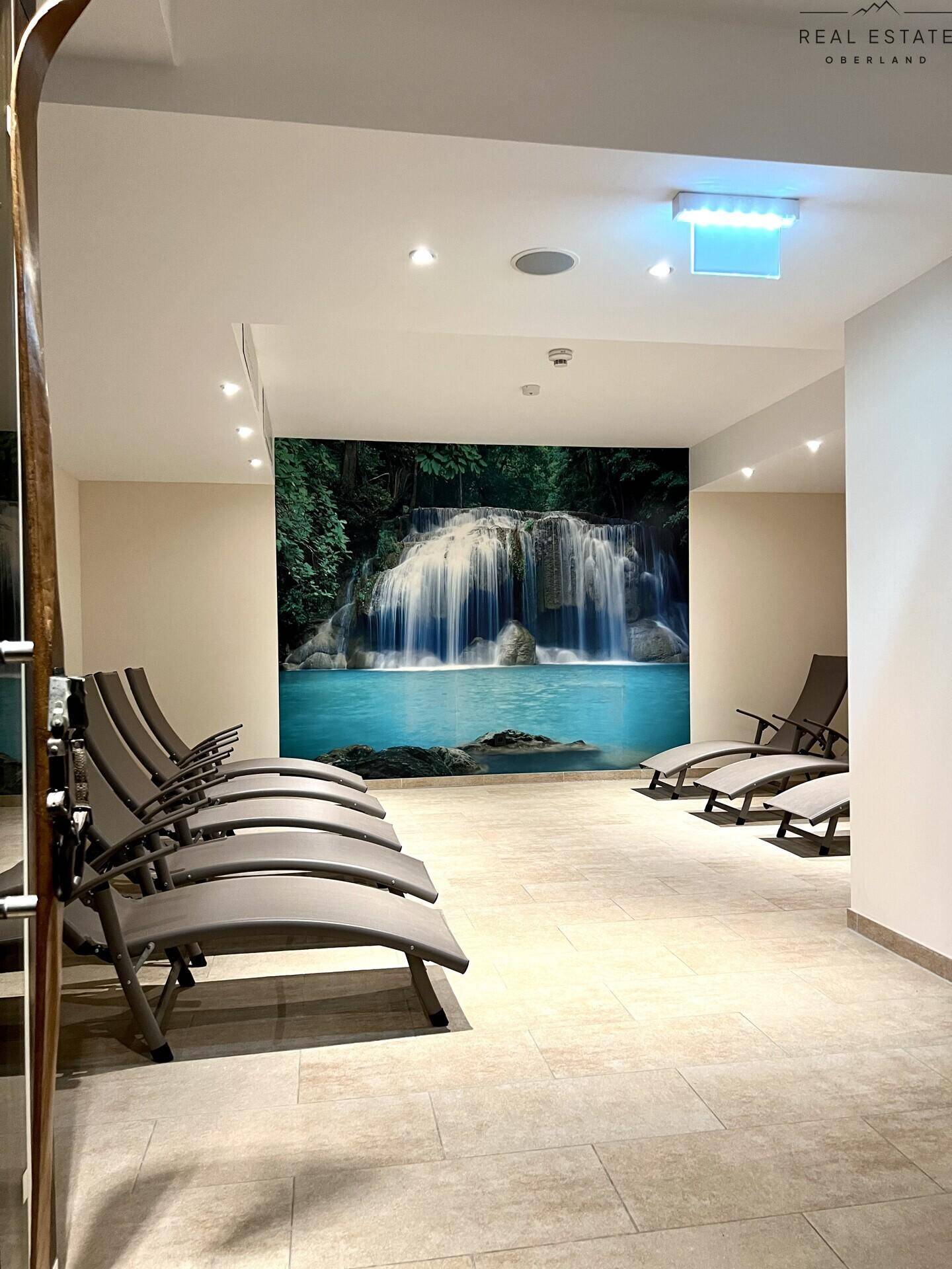Entspannungsbereich mit Liegen und einer Wandtapete, die einen Wasserfall darstellt.