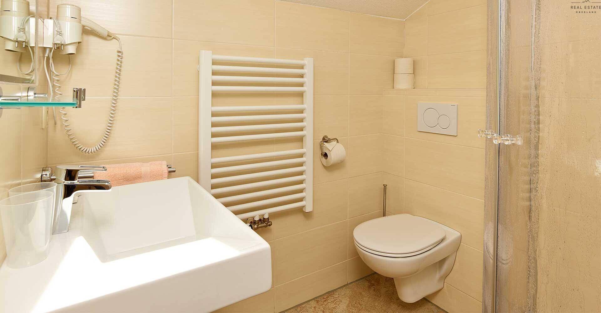 Helles Badezimmer mit beigen Fliesen, wandhängendem WC und Duschkabine.