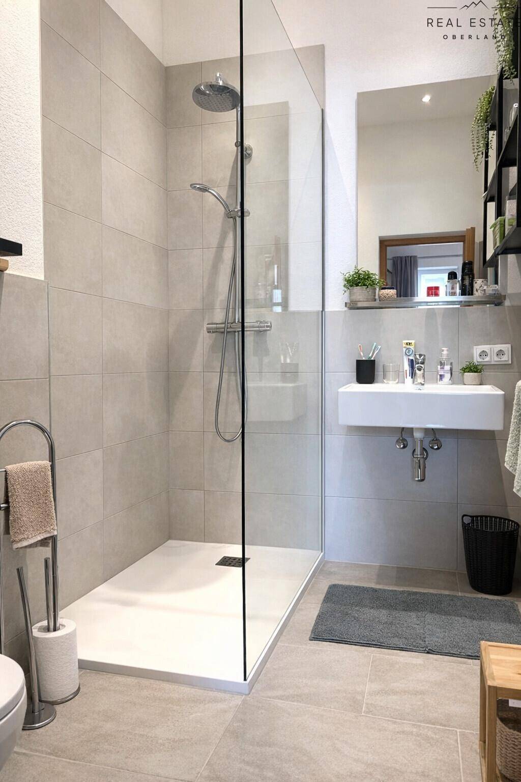 Modernes Badezimmer mit ebenerdiger Dusche, Waschbecken und großem Spiegel, hell gefliest.