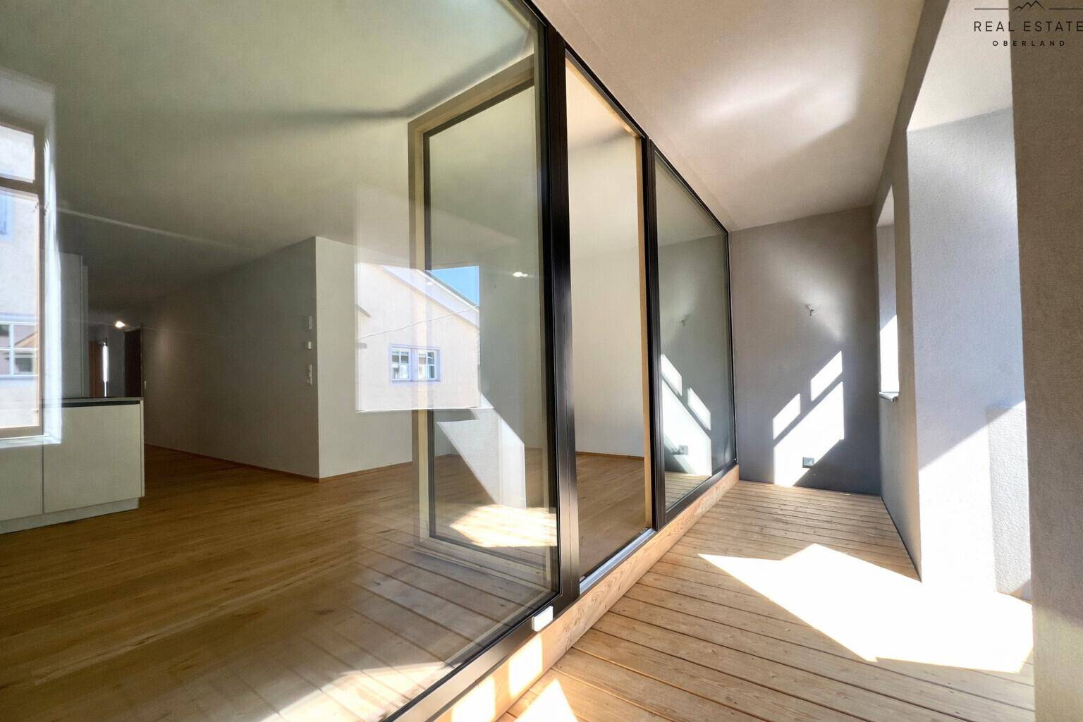 Heller Außenbereich mit Holzfußboden und großer Glasfront zum Innenraum der Wohnung.