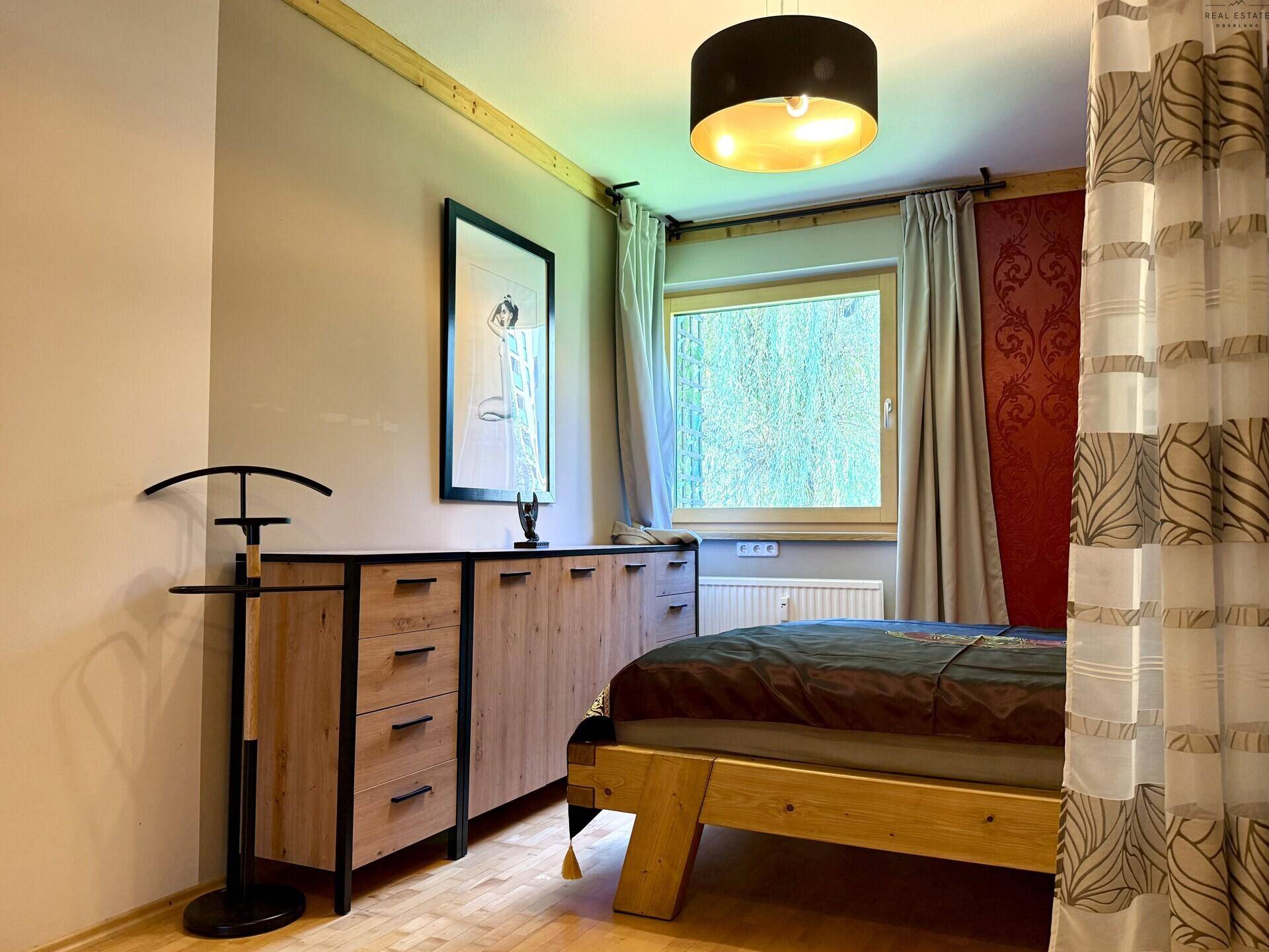 Schlafzimmer mit Holzboden, Fenster und modernem Sideboard.