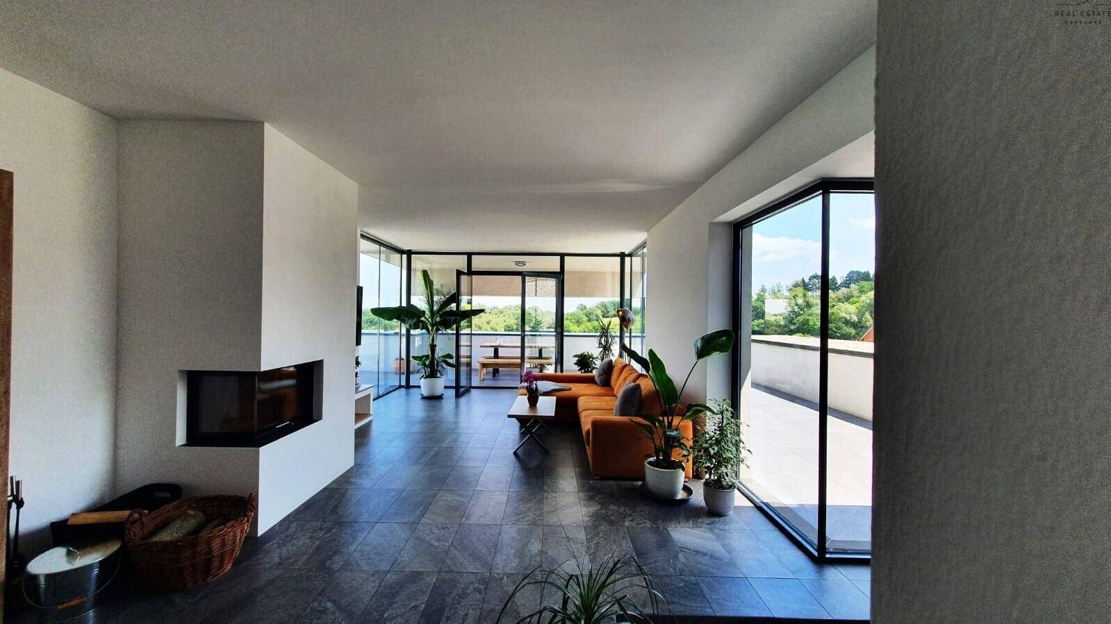Moderner Wohnbereich mit großen Fenstern, dunklem Fliesenboden und integriertem Kamin mit Zugang zur Terrasse.
