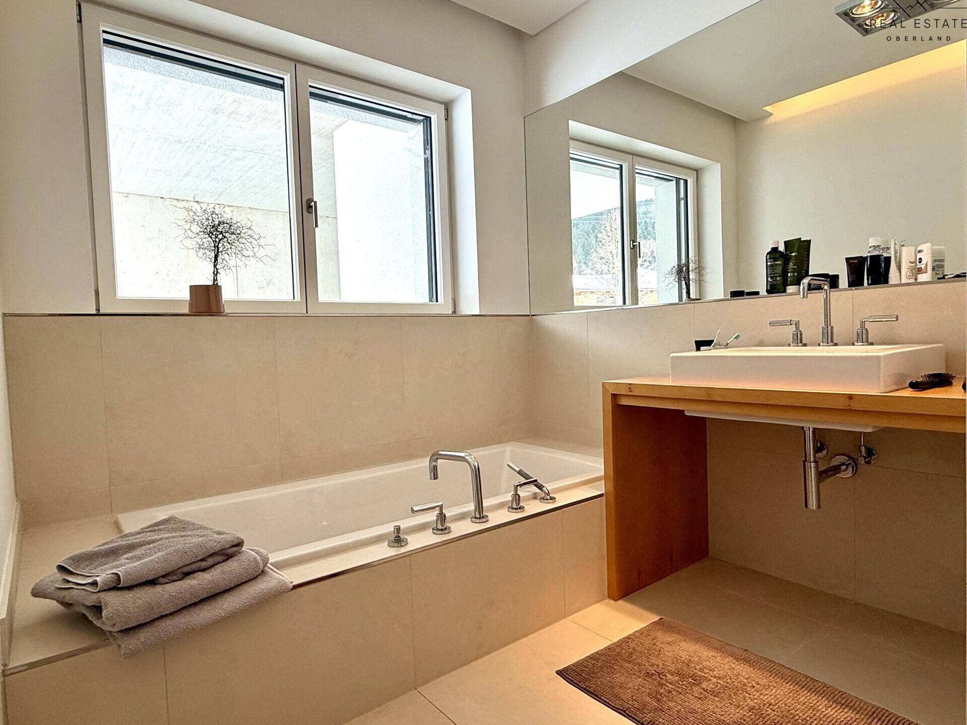 Helles Badezimmer mit eingebauter Badewanne, modernem Waschbecken und großem Spiegel.
