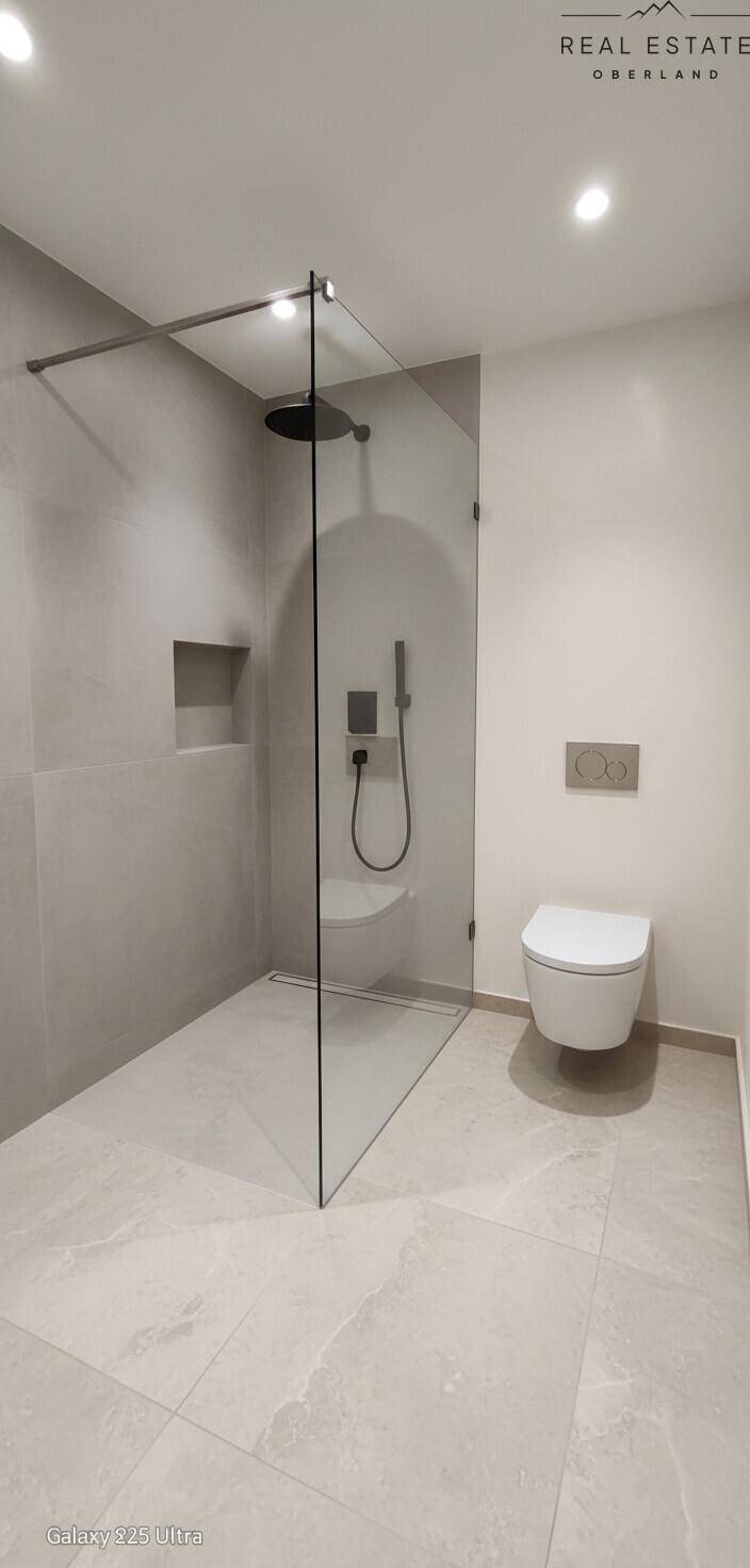 Modernes Badezimmer mit begehbarer Dusche, Wand-WC und großen Fliesen.