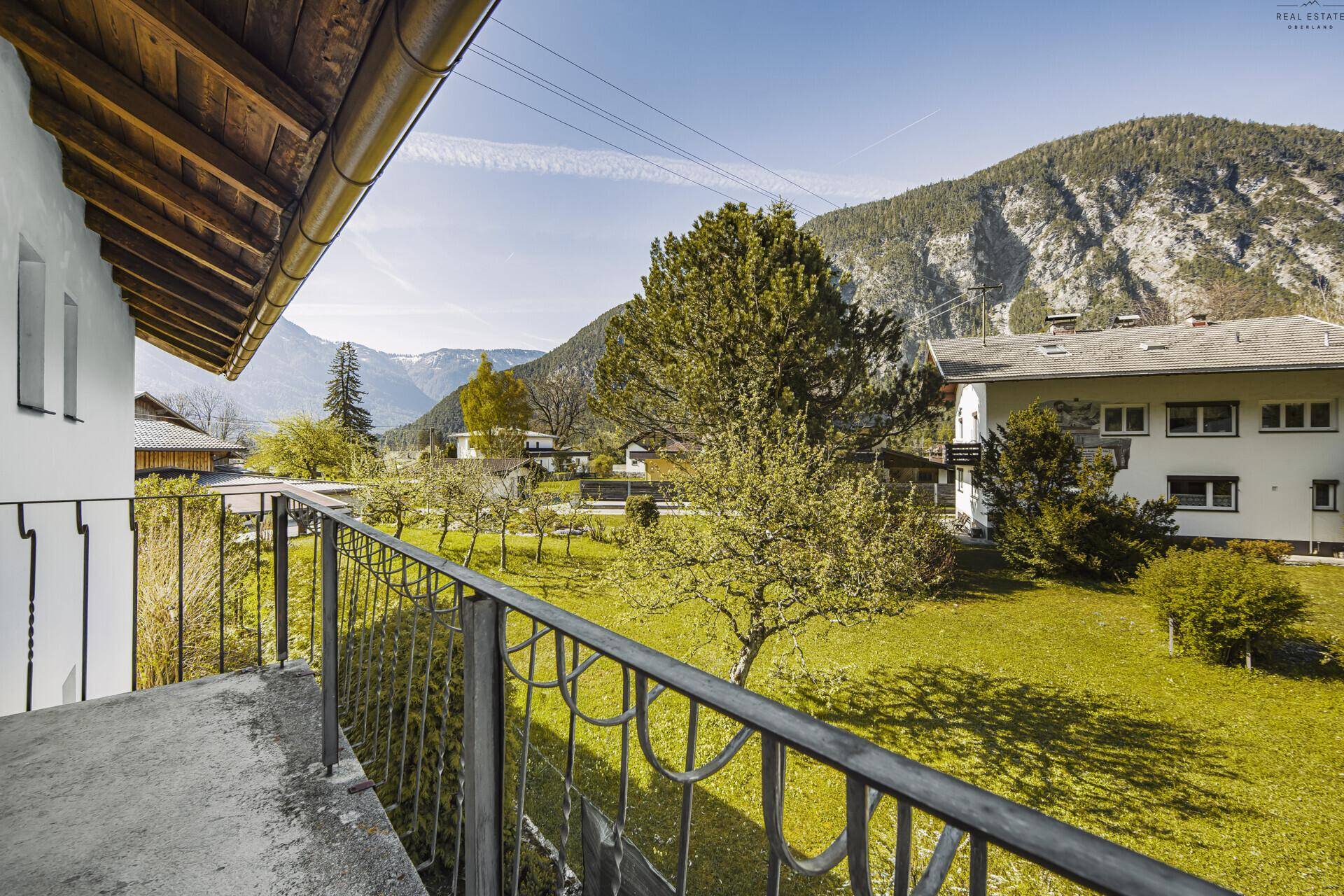 Balkon mit Blick auf den grünen Garten und die umliegende Berglandschaft.